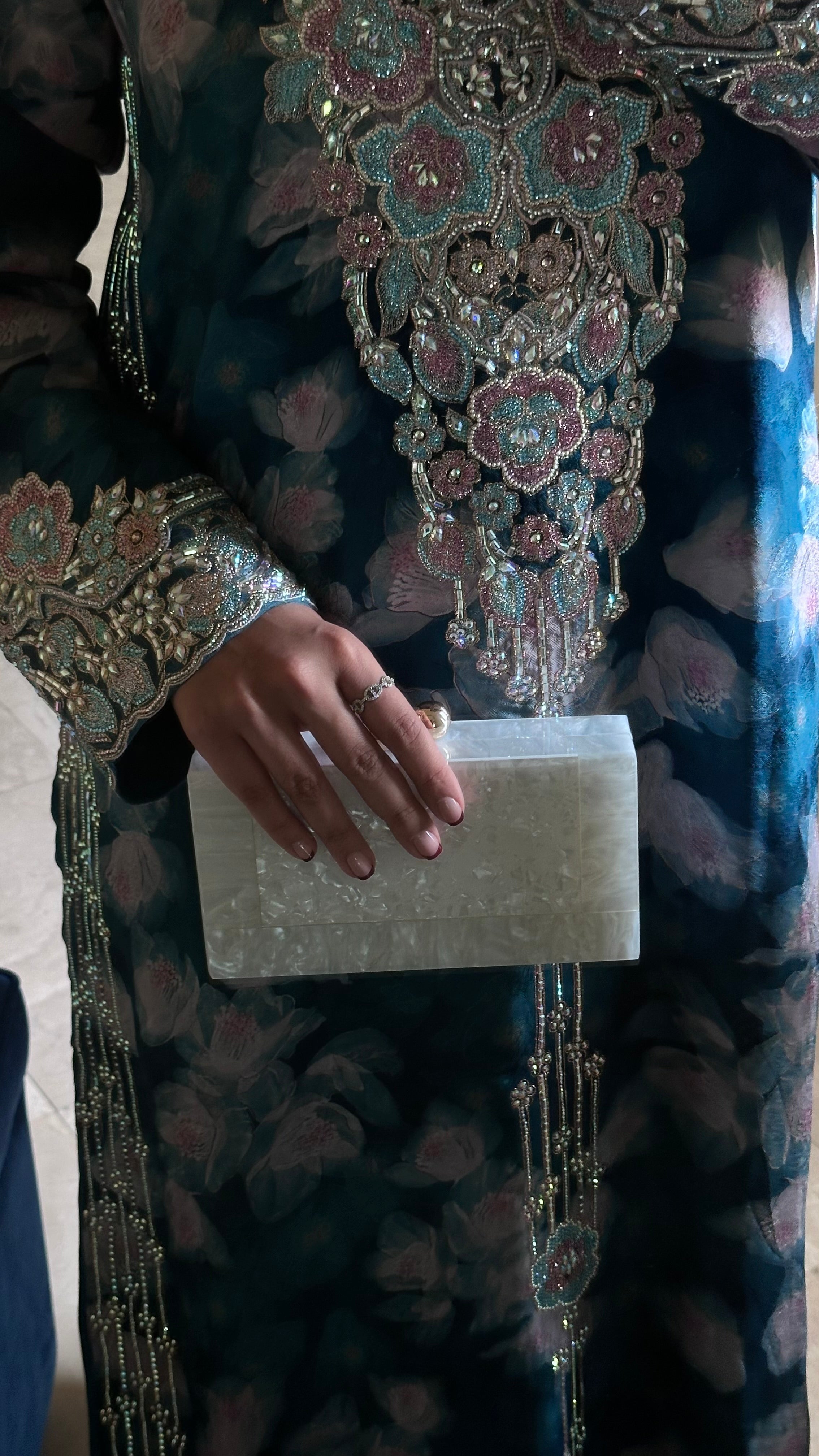 Person wearing a detailed traditional outfit holding a white clutch.