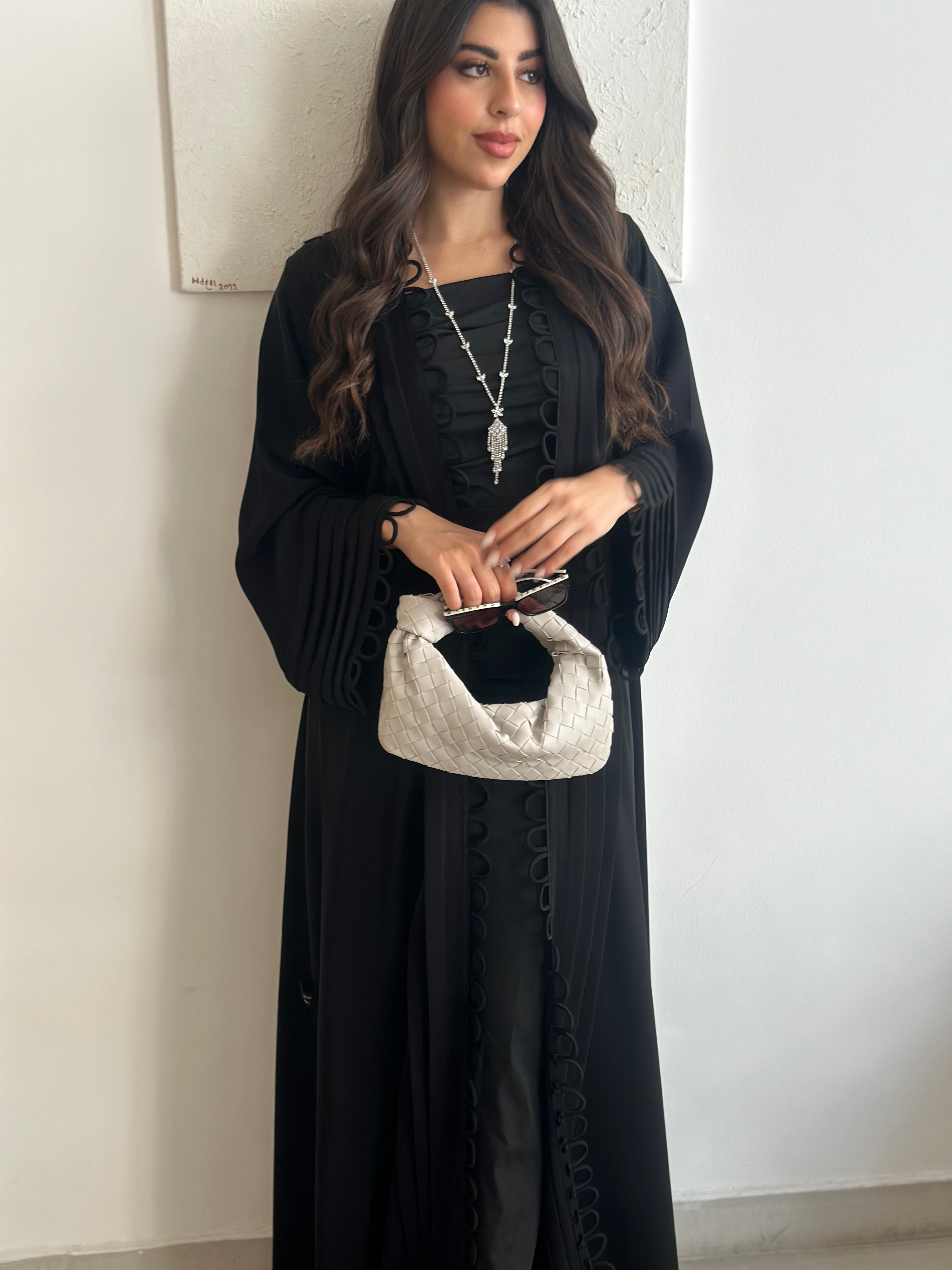 Woman in a black dress holding a white clutch against a plain background