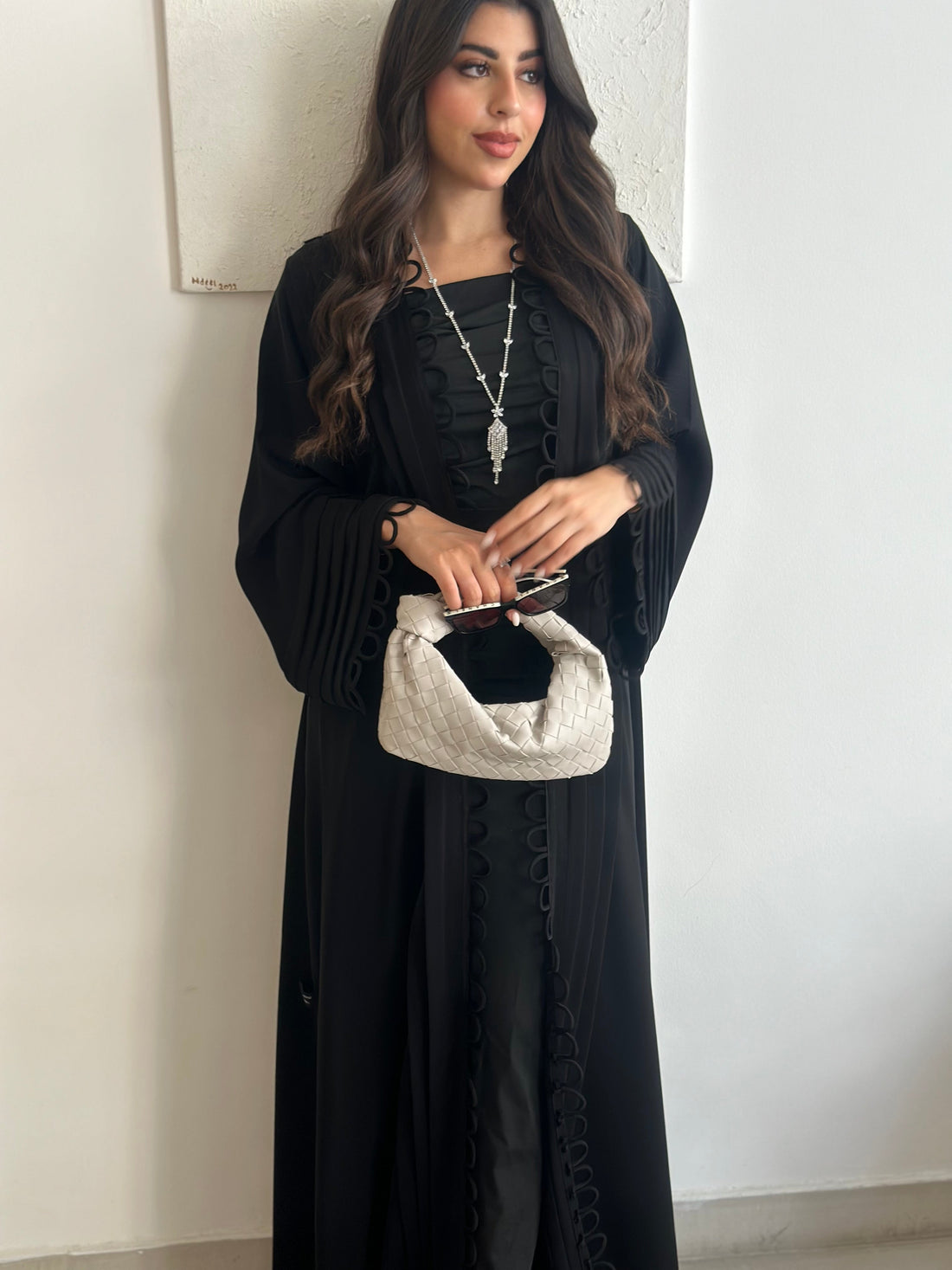 Woman in a black dress holding a white clutch against a plain background