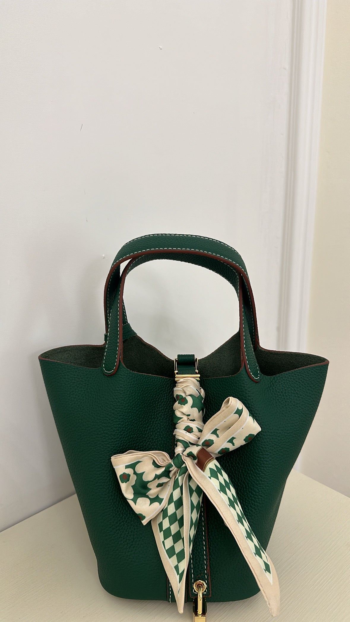 A green leather clutch bag with a gold finish padlock and a decorative scarf tied to it.