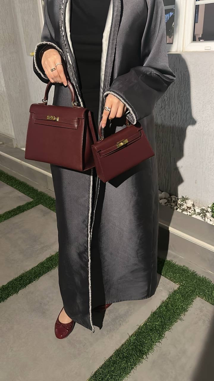 Person holding two maroon handbags against a gray wall.