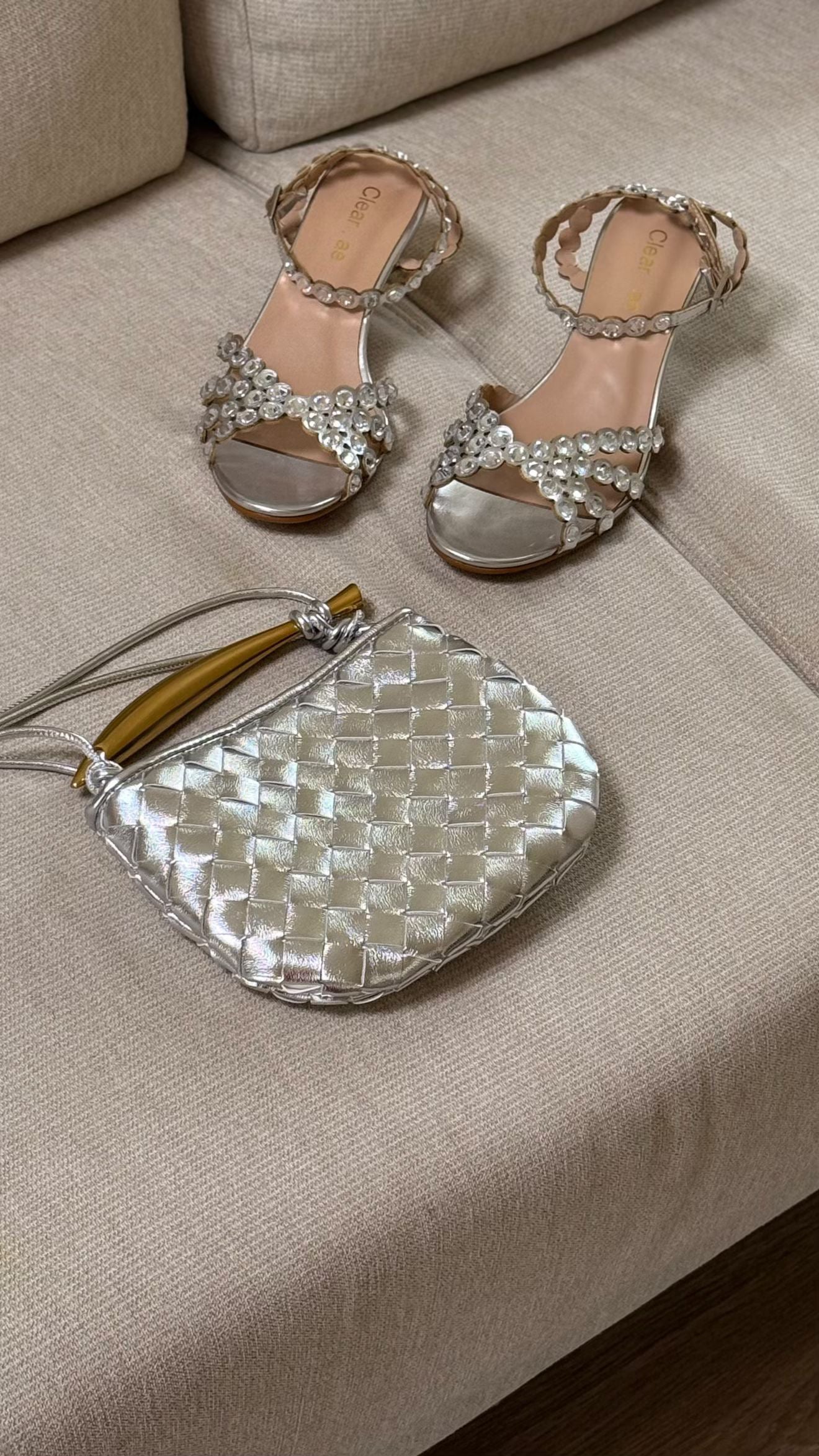 Pair of silver high-heeled sandals with a matching handbag on a beige surface