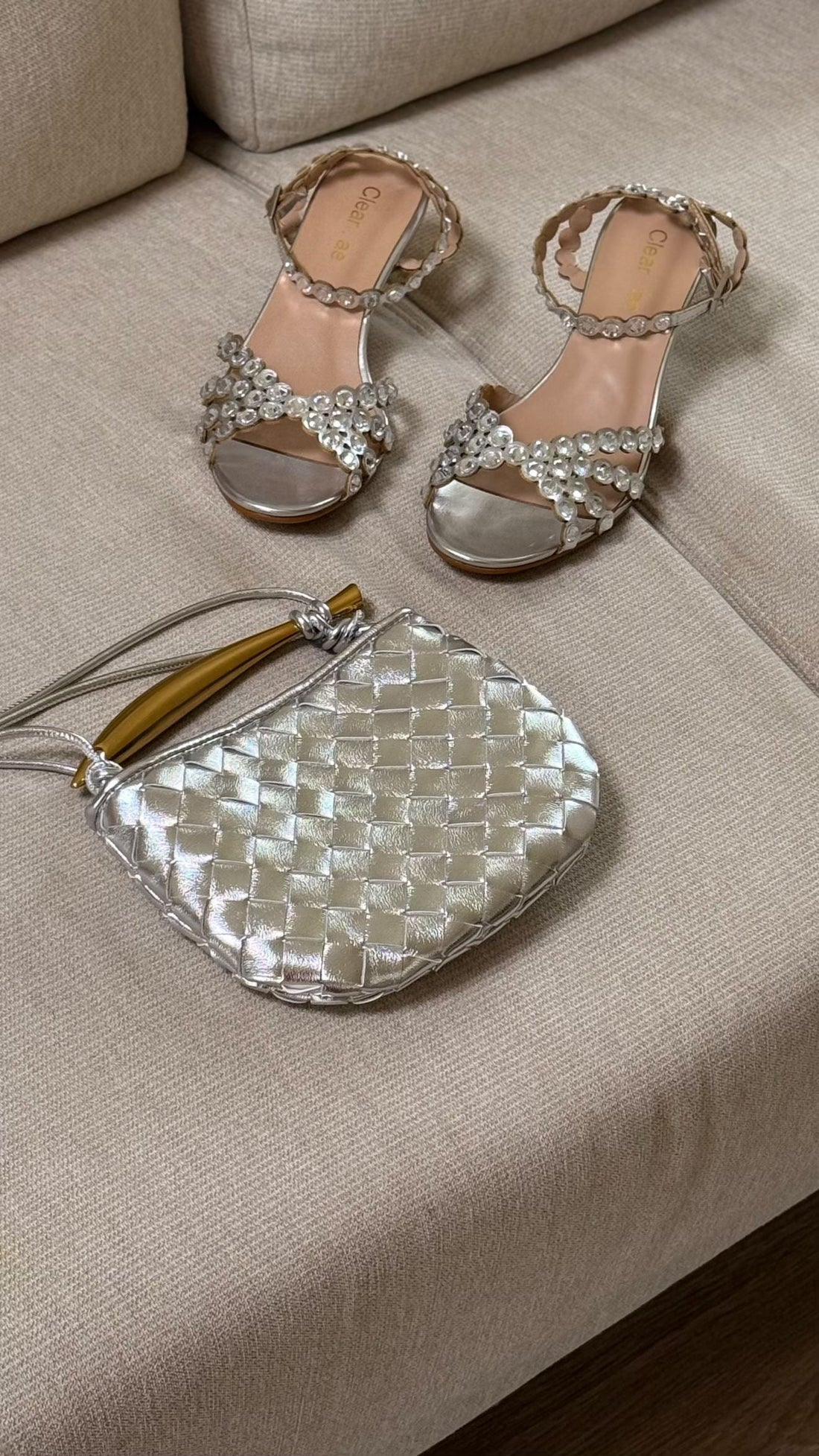 Pair of silver high-heeled sandals with a matching handbag on a beige surface