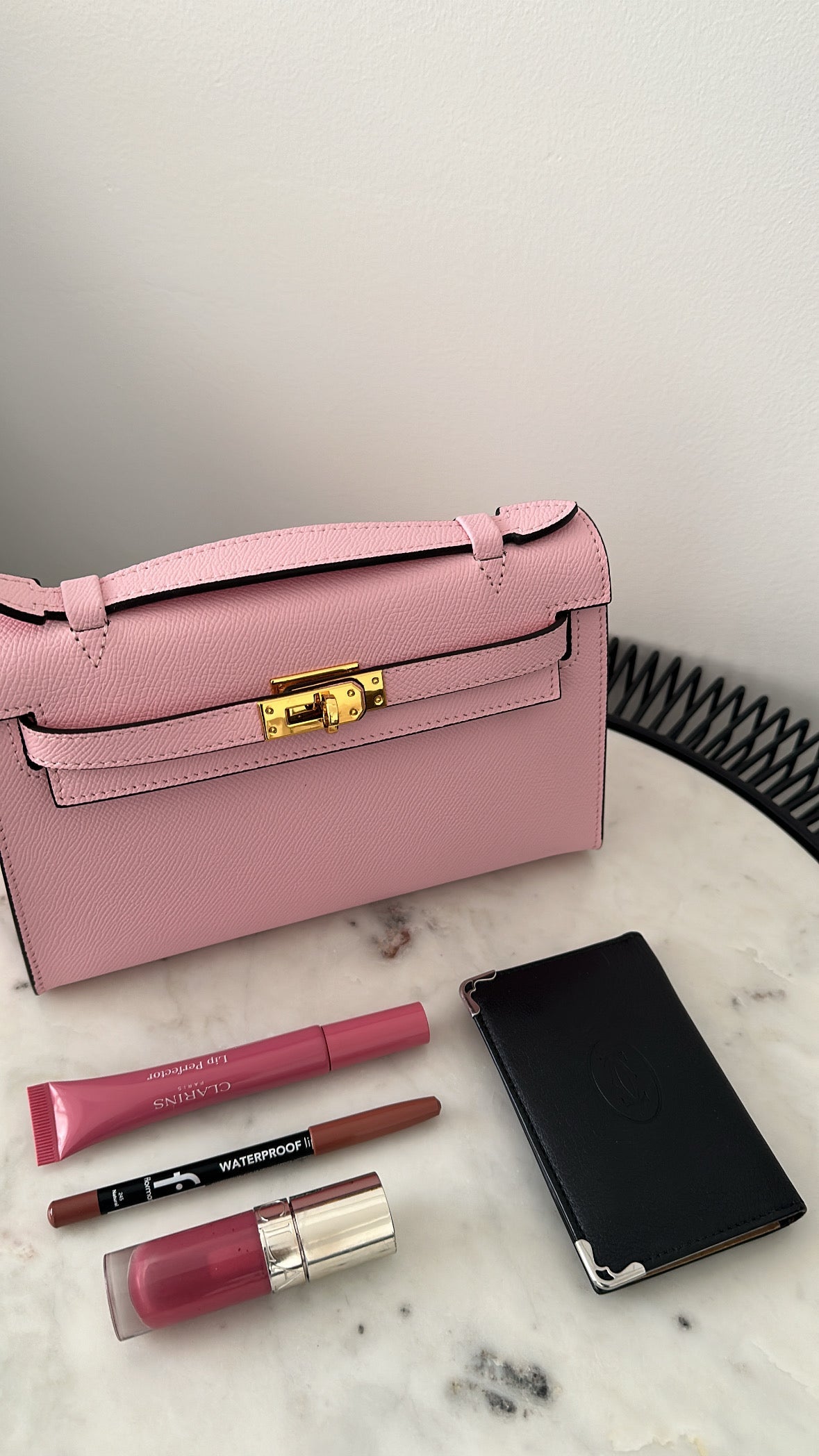 Pink handbag with makeup items on a marble surface