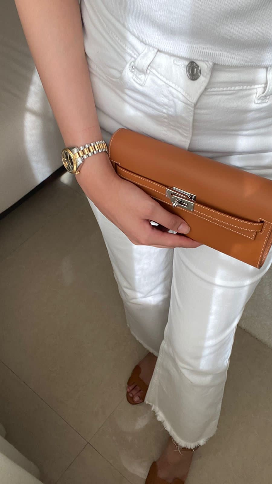 Person holding a brown clutch with white pants and gold watch
