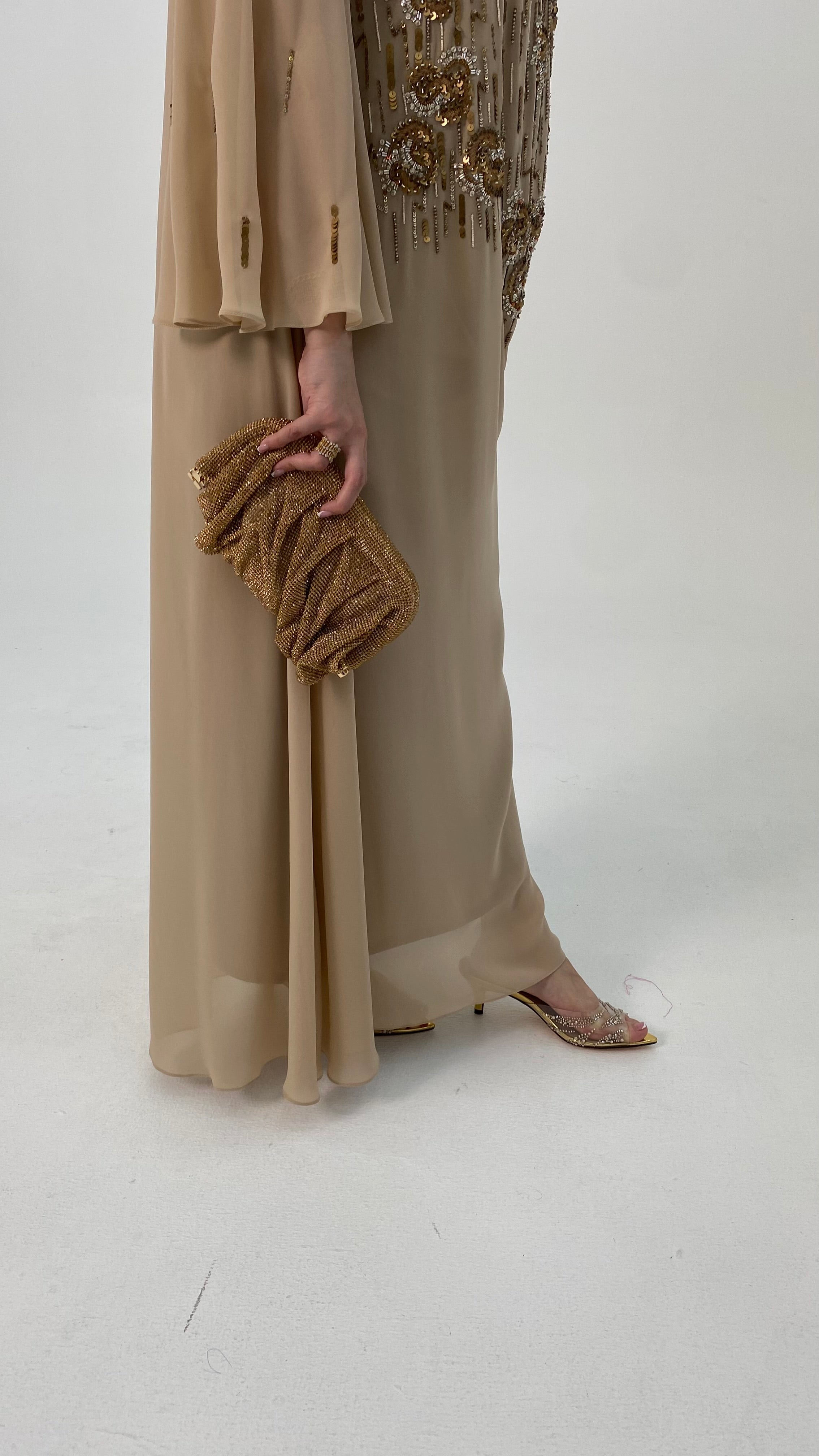 Person wearing a beige outfit with a floral top and holding a matching clutch against a white background