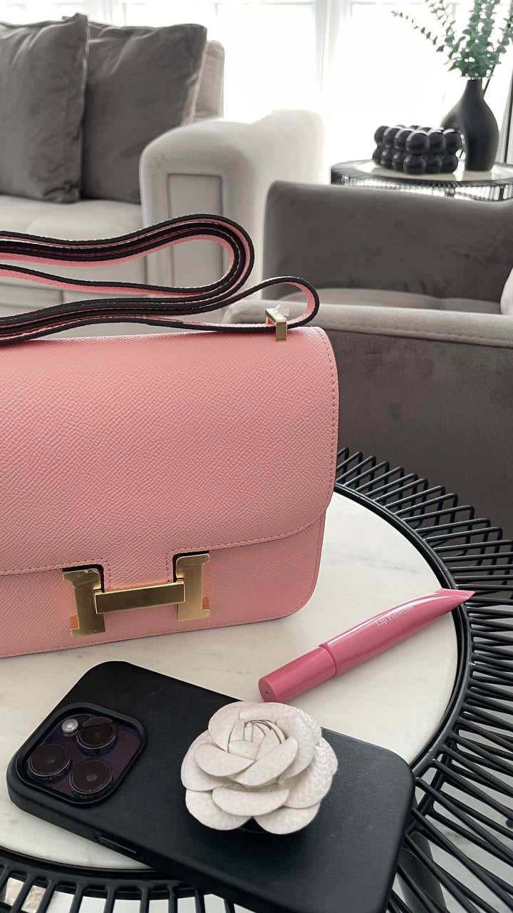 Pink handbag on a white surface with a phone, pen, and decorative item.