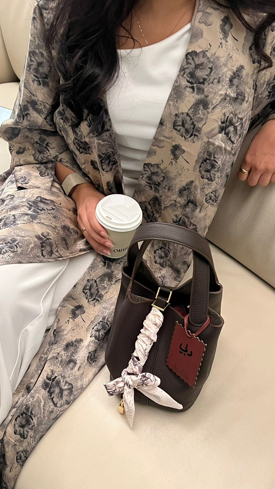 Person holding a coffee cup with a brown handbag on a light-colored couch