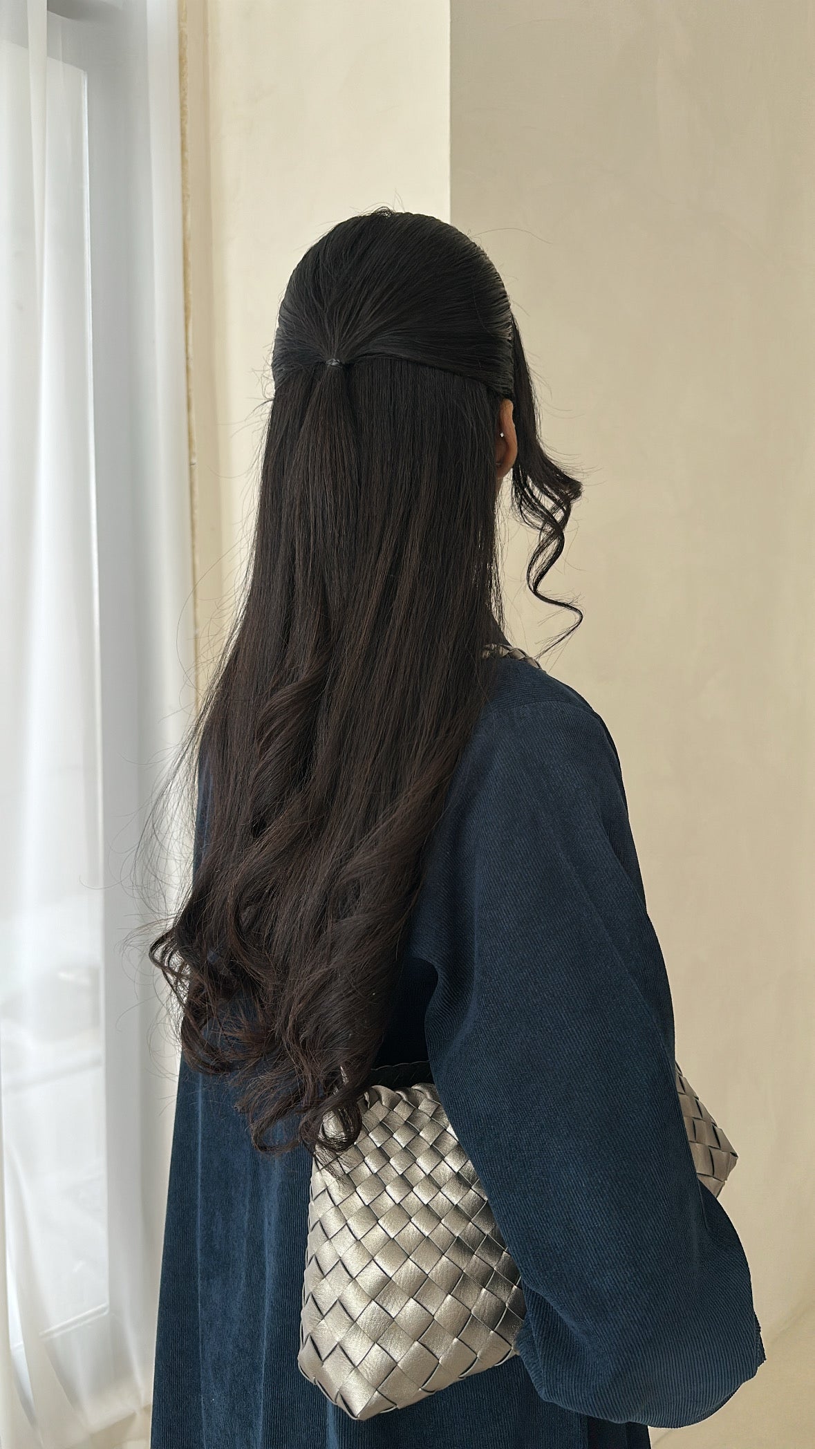 Woman with long dark hair wearing a blue outfit and holding a woven handbag.