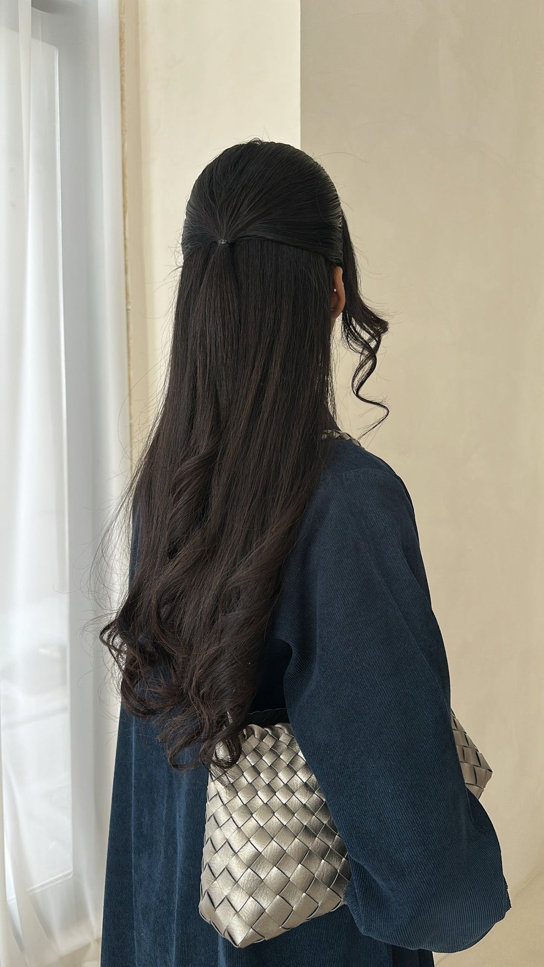 Woman with long dark hair wearing a blue outfit and holding a woven handbag.