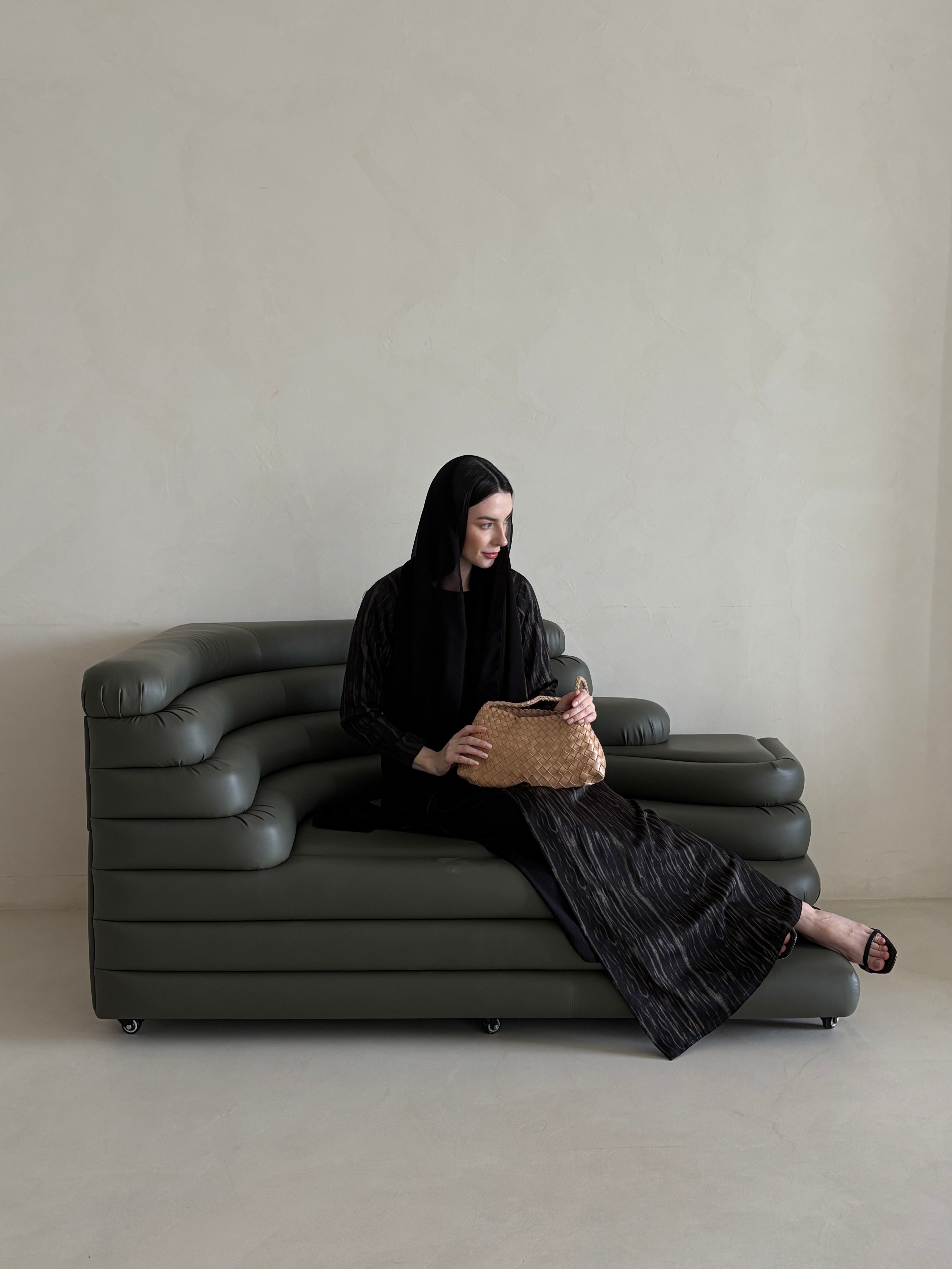 Person sitting on a modern gray sofa holding a woven bag against a plain background