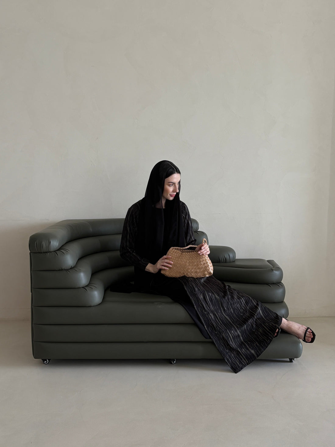 Person sitting on a modern gray sofa holding a woven bag against a plain background