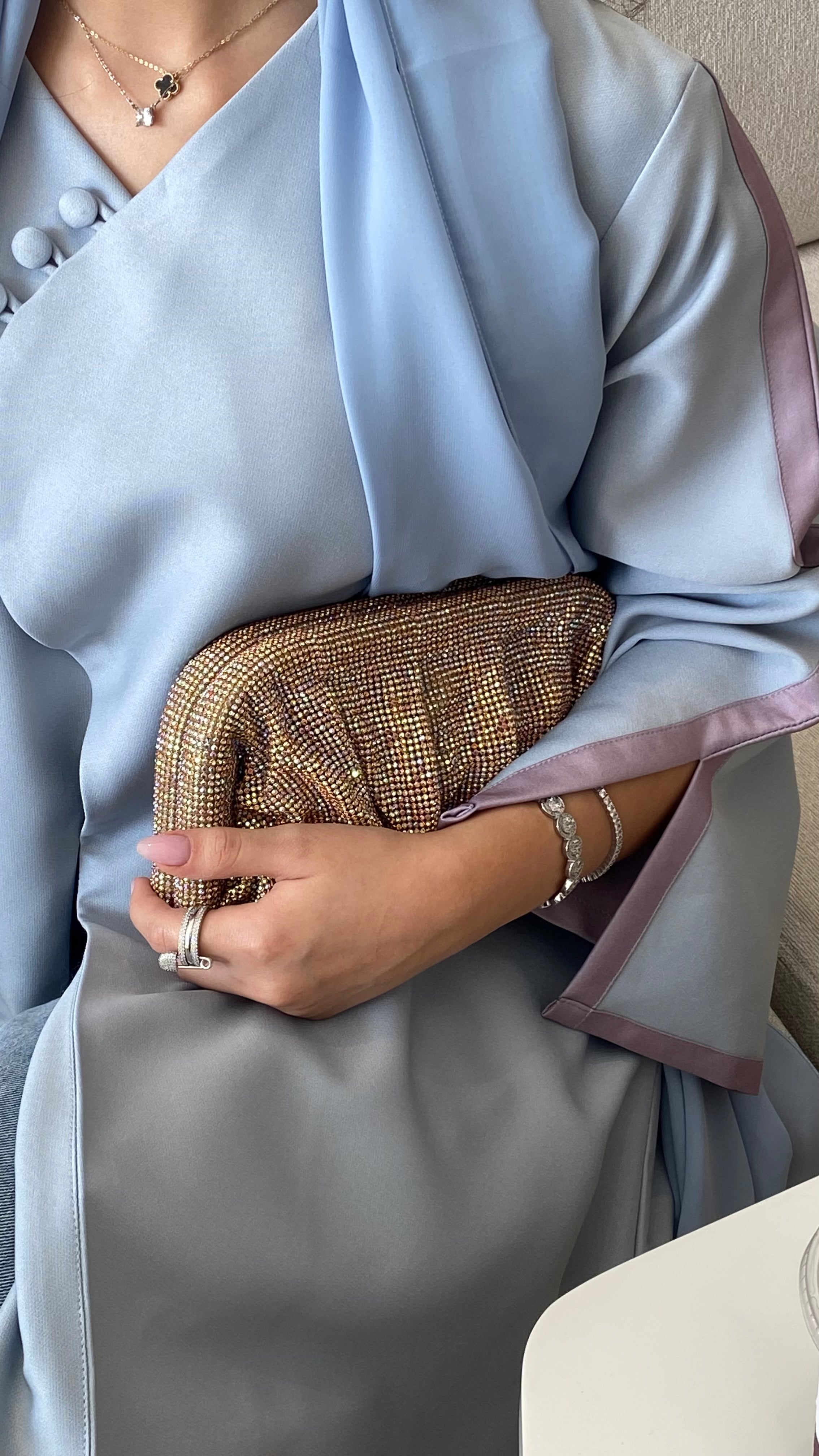 Person holding a gold clutch wearing a light blue top and gray skirt.