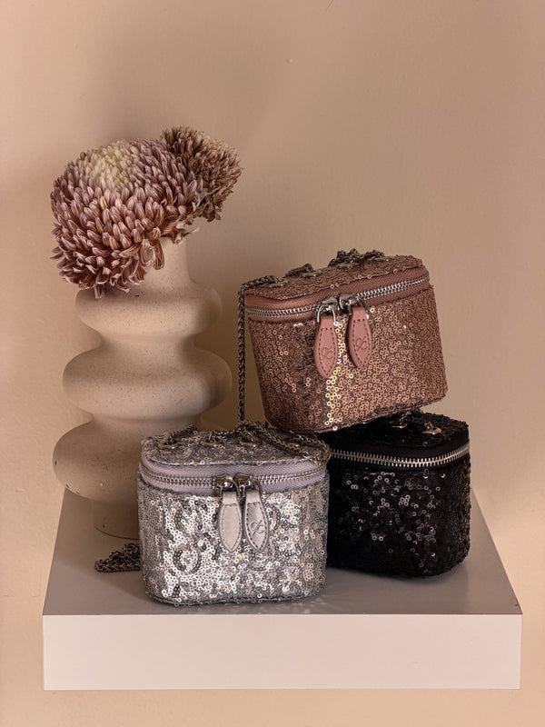 Three decorative boxes with sequin patterns on a beige surface with a decorative plant.