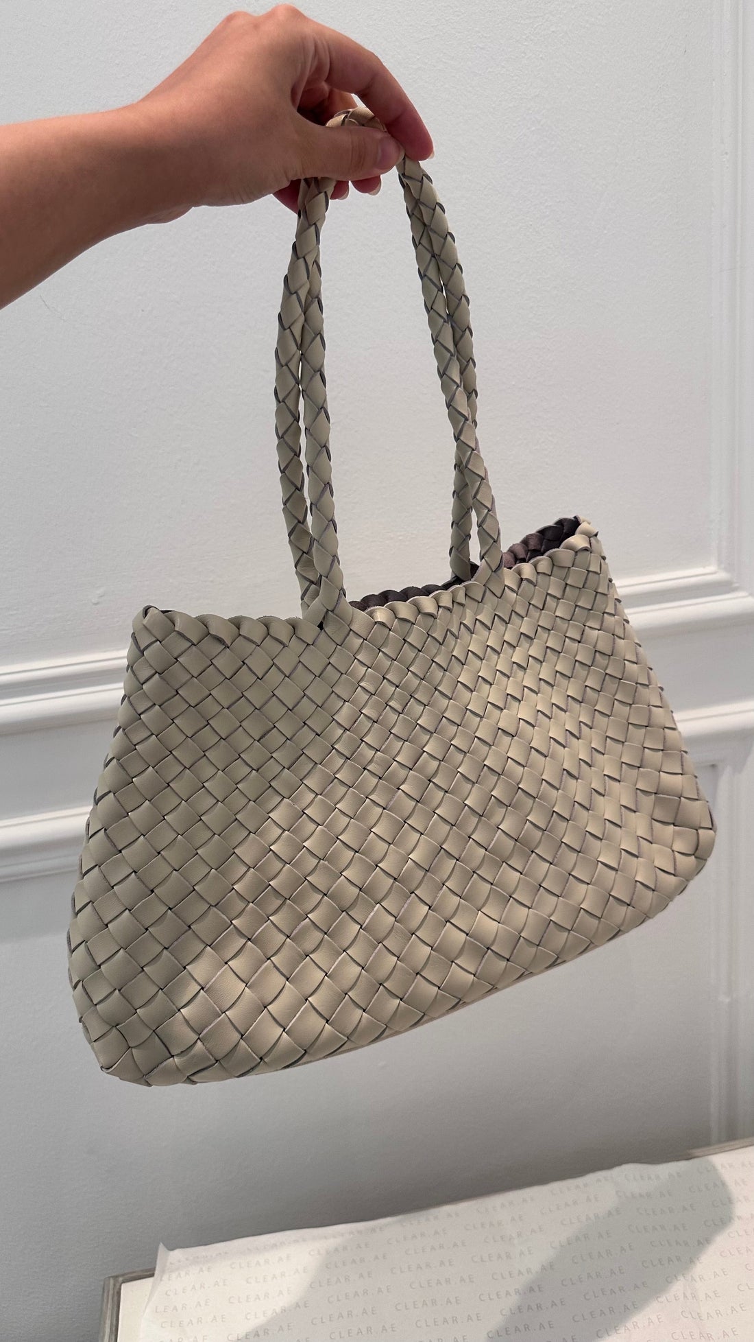 Hand holding a woven beige handbag against a light background