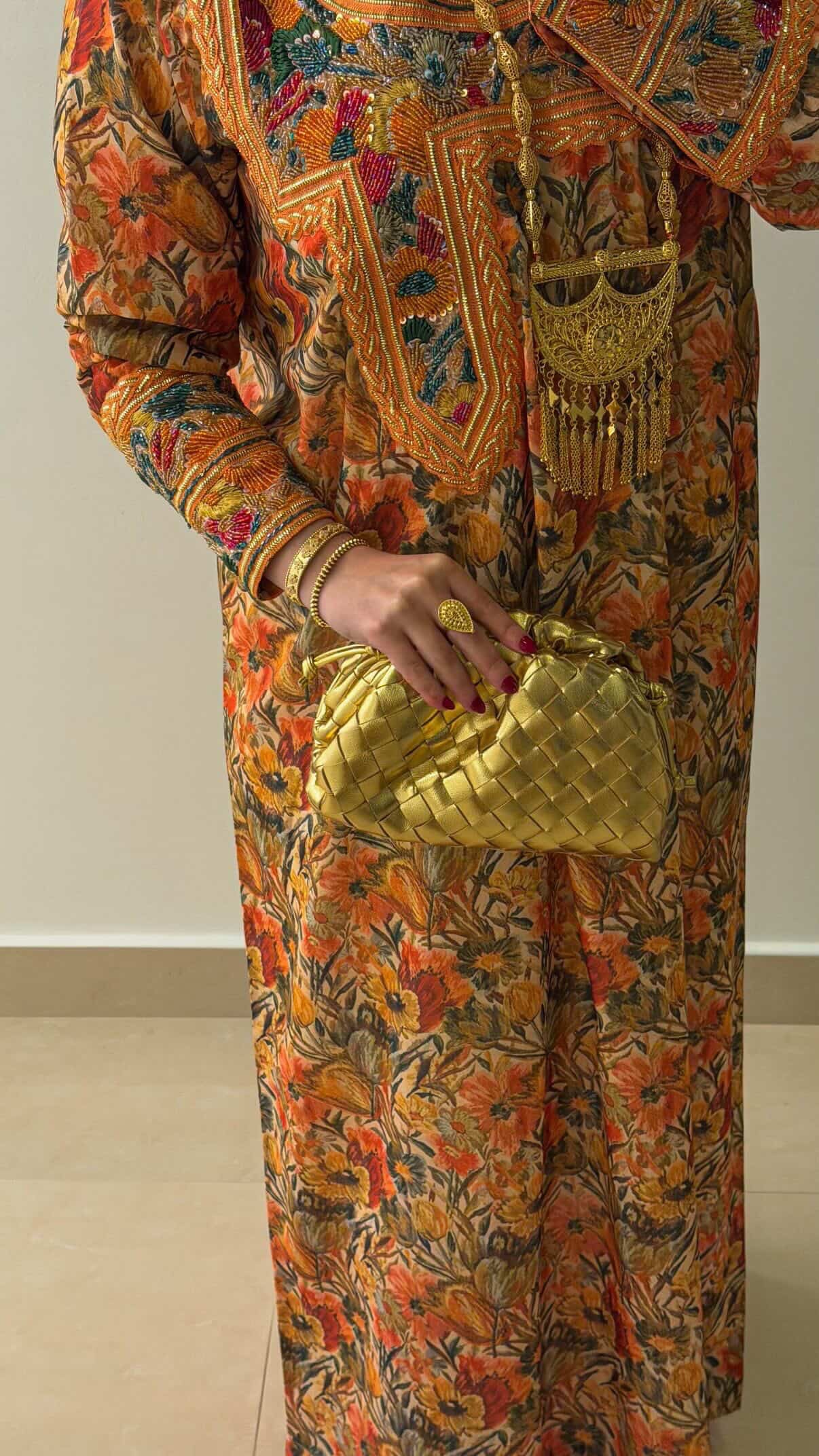Person wearing a colorful patterned outfit holding a gold clutch.