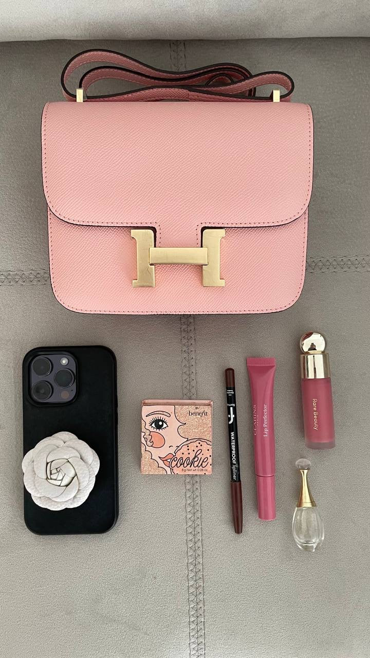 Pink handbag with phone, makeup items on a gray surface
