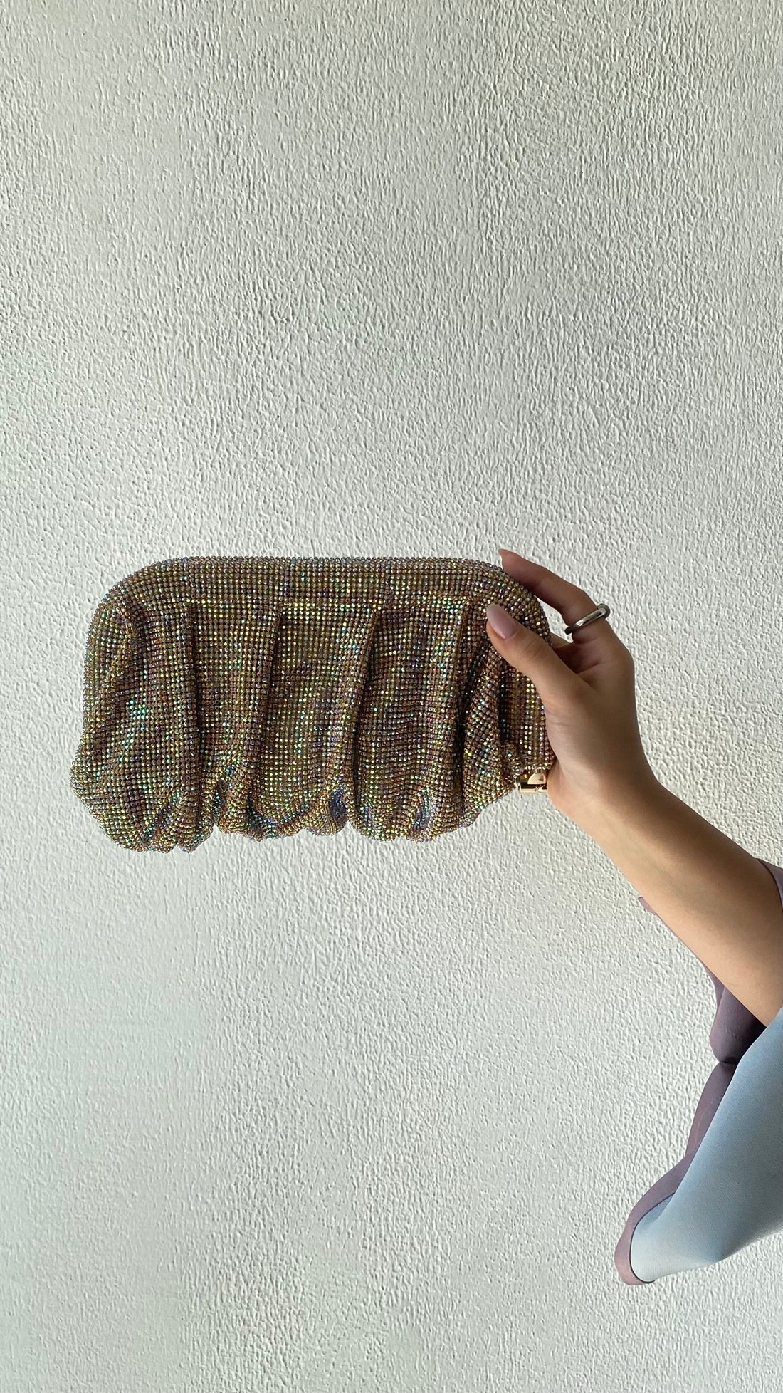 Hand holding a textured clutch against a plain background
