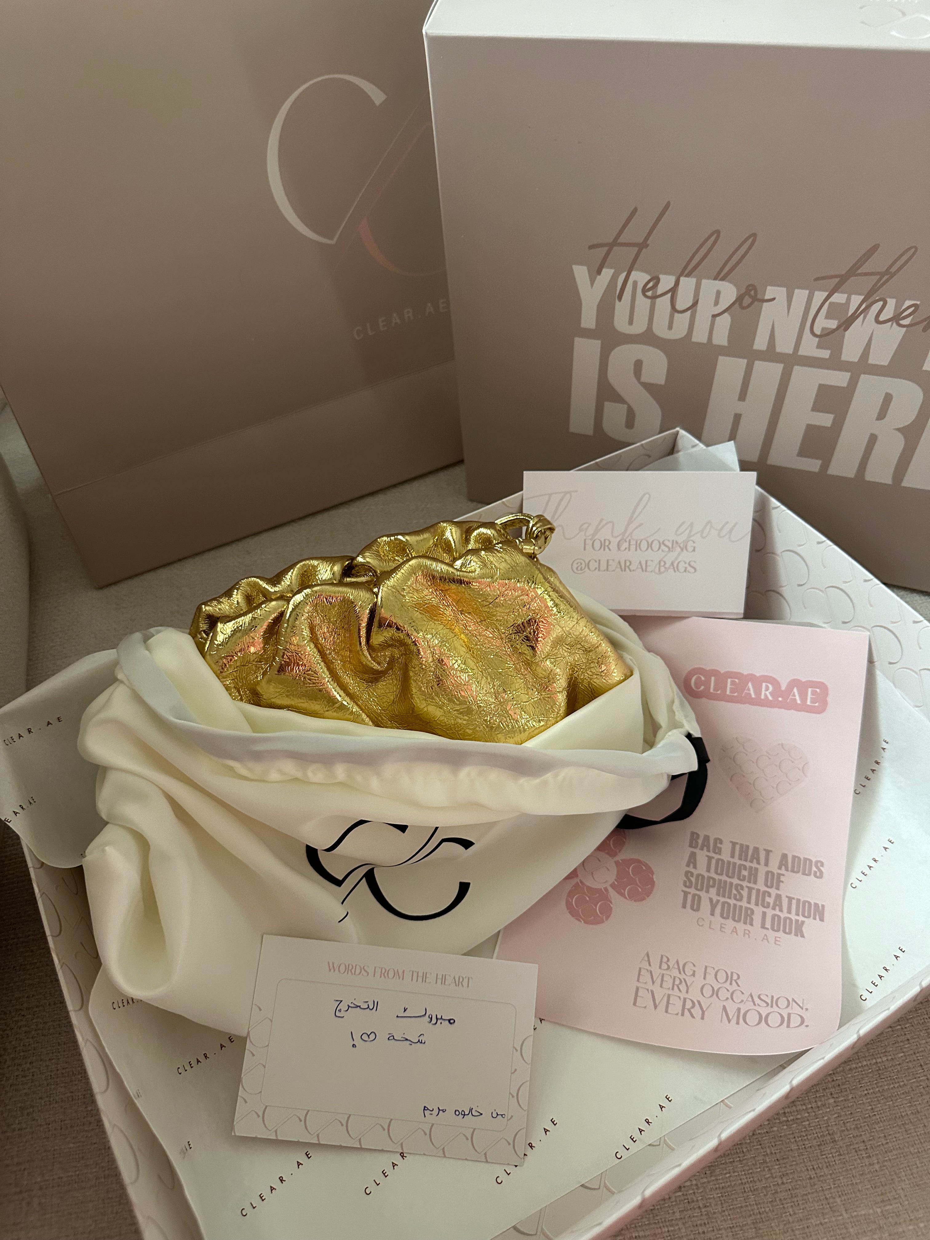 An open gift box containing a golden scarf, a white handbag, a card, and a thank you note.