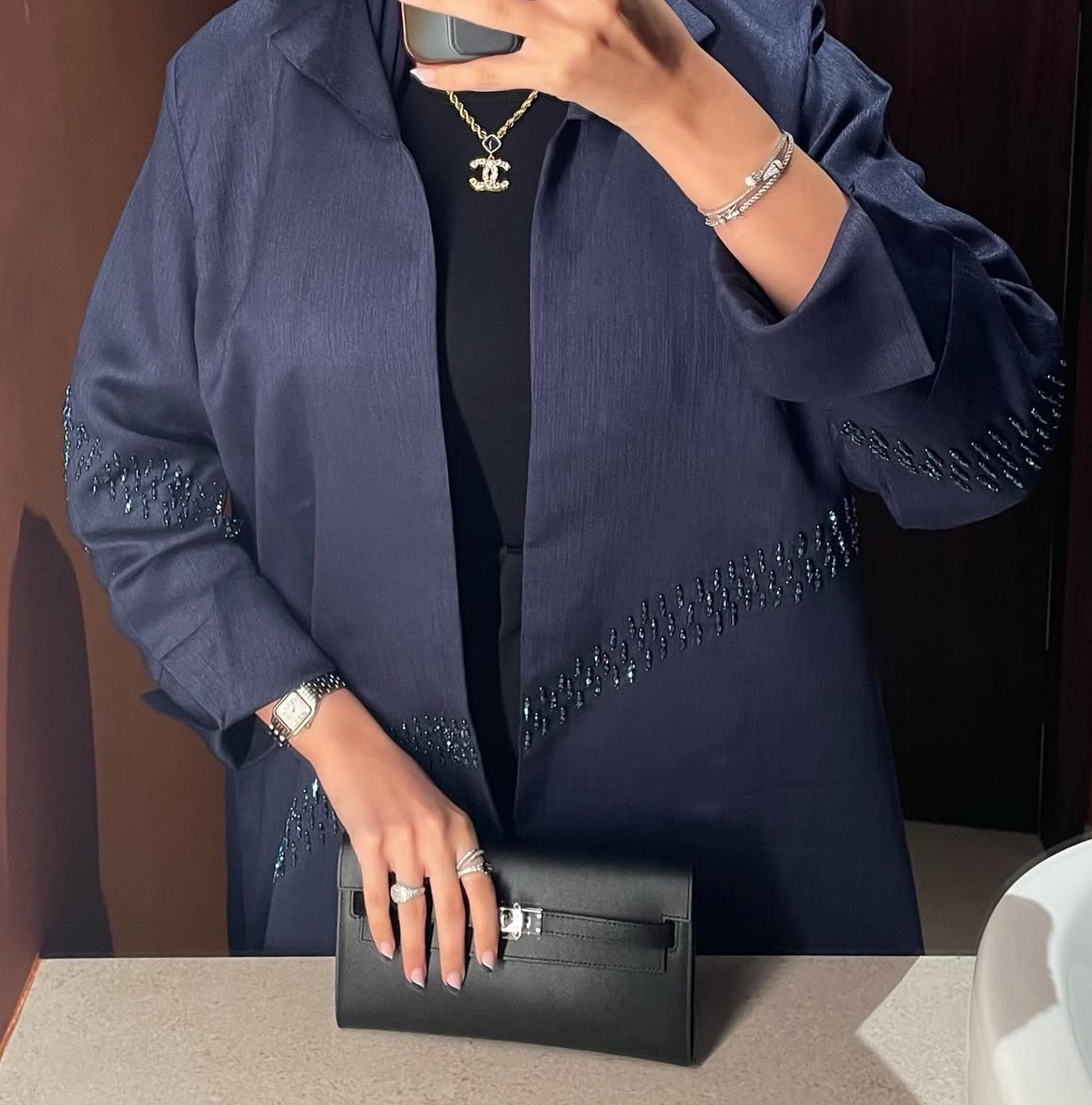 Person wearing a dark blue outfit with beaded details, holding a black clutch.