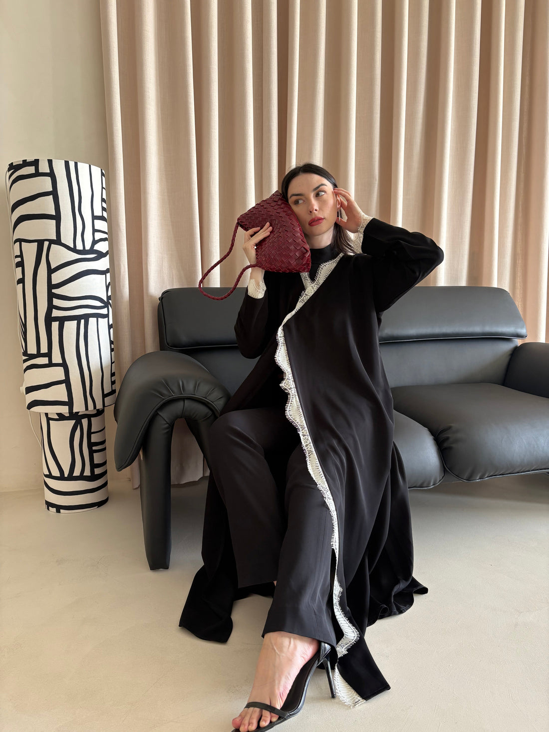Woman sitting on a couch holding a red handbag, wearing a black outfit with white trim.