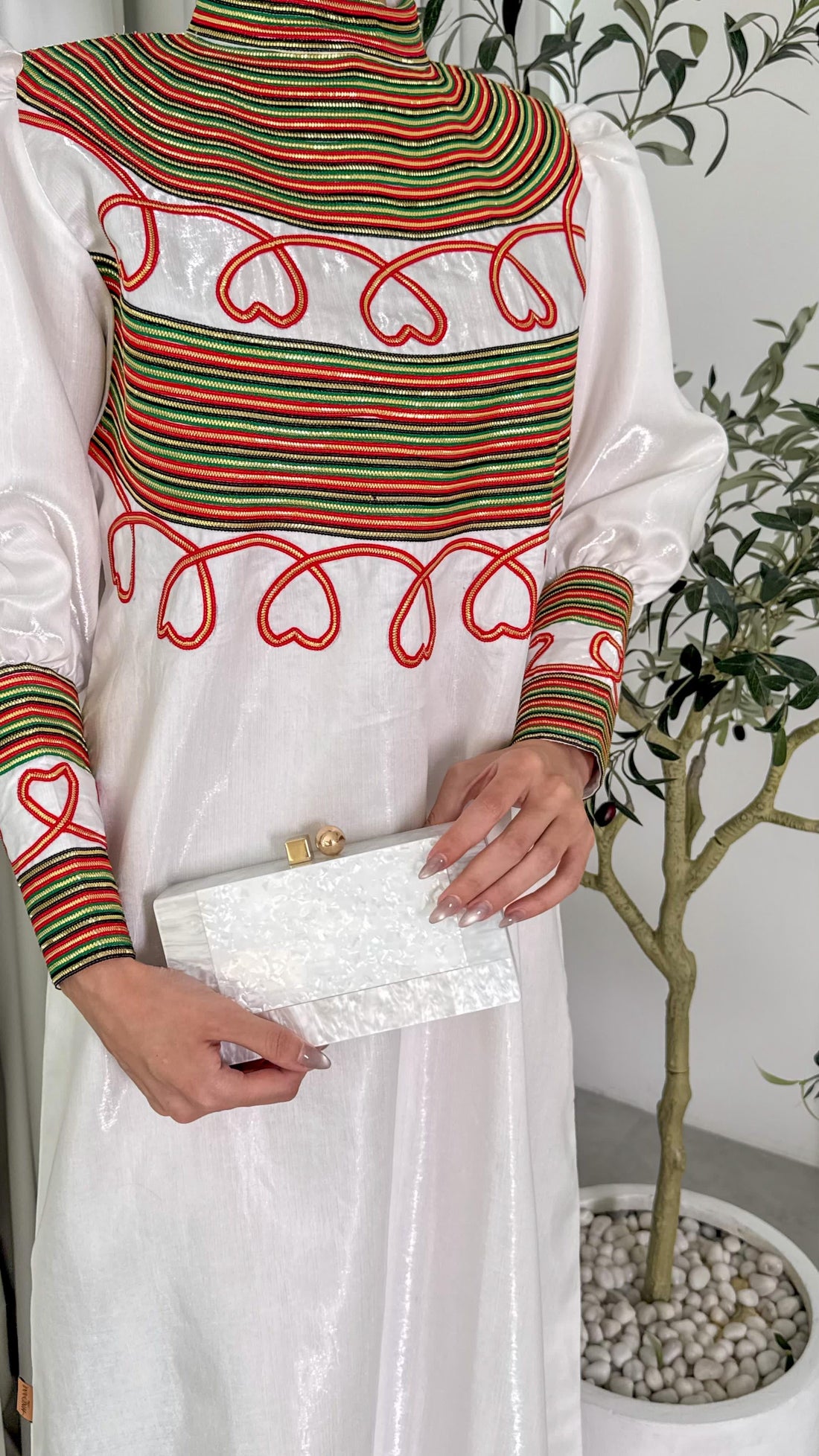 Person wearing a colorful top with red, green, and white patterns holding a white clutch.