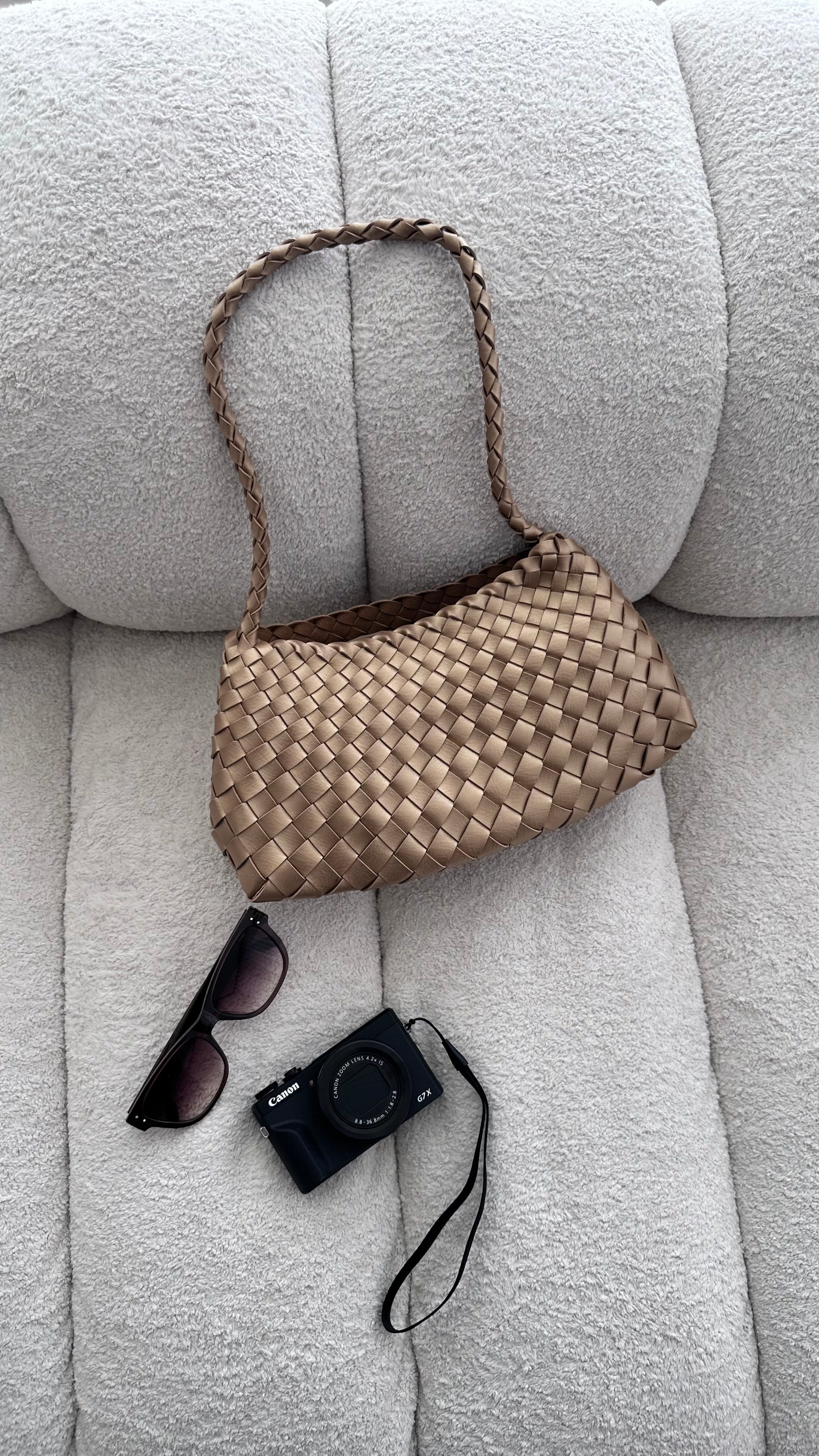 Woven handbag, sunglasses, and camera on a light gray sofa