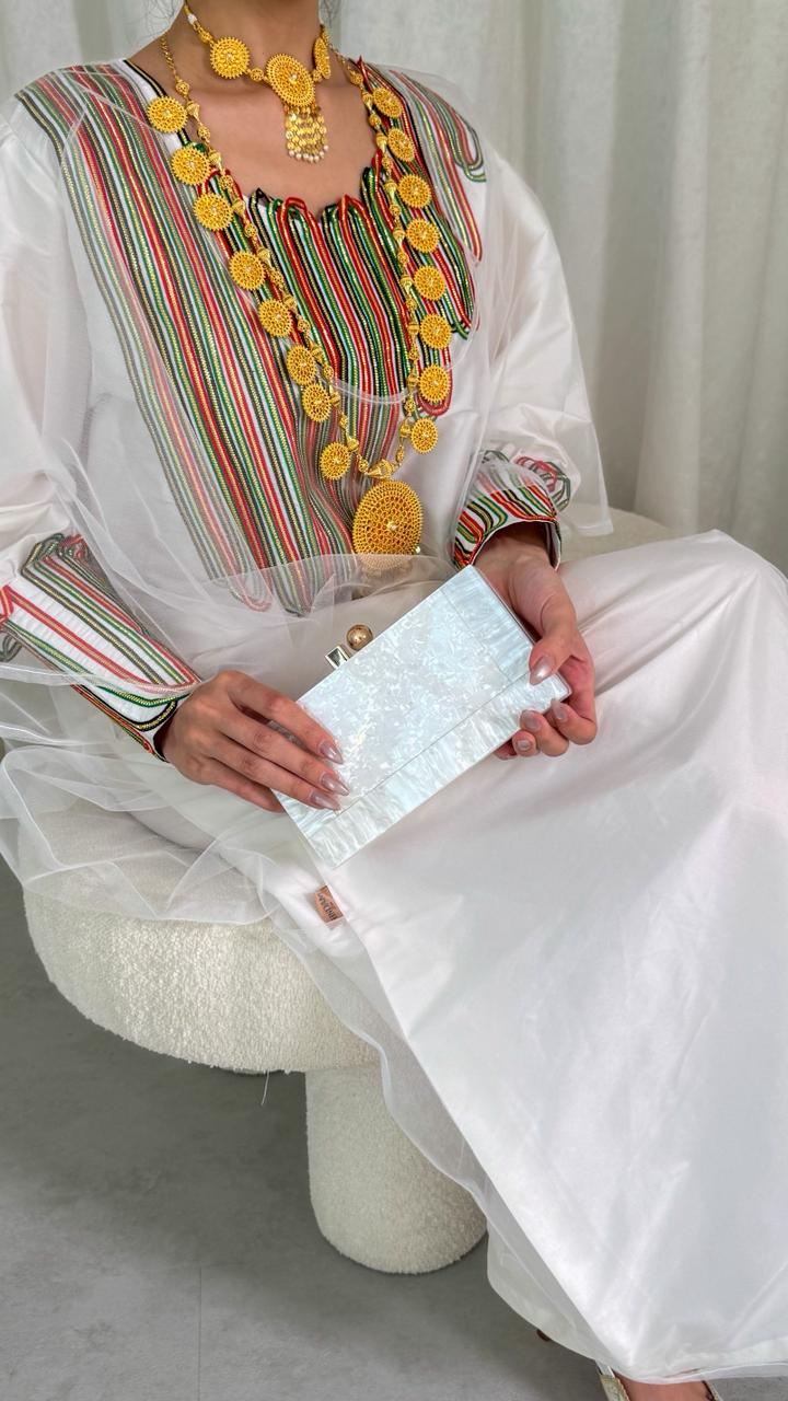 Person wearing traditional attire with colorful embroidery and holding a white clutch.