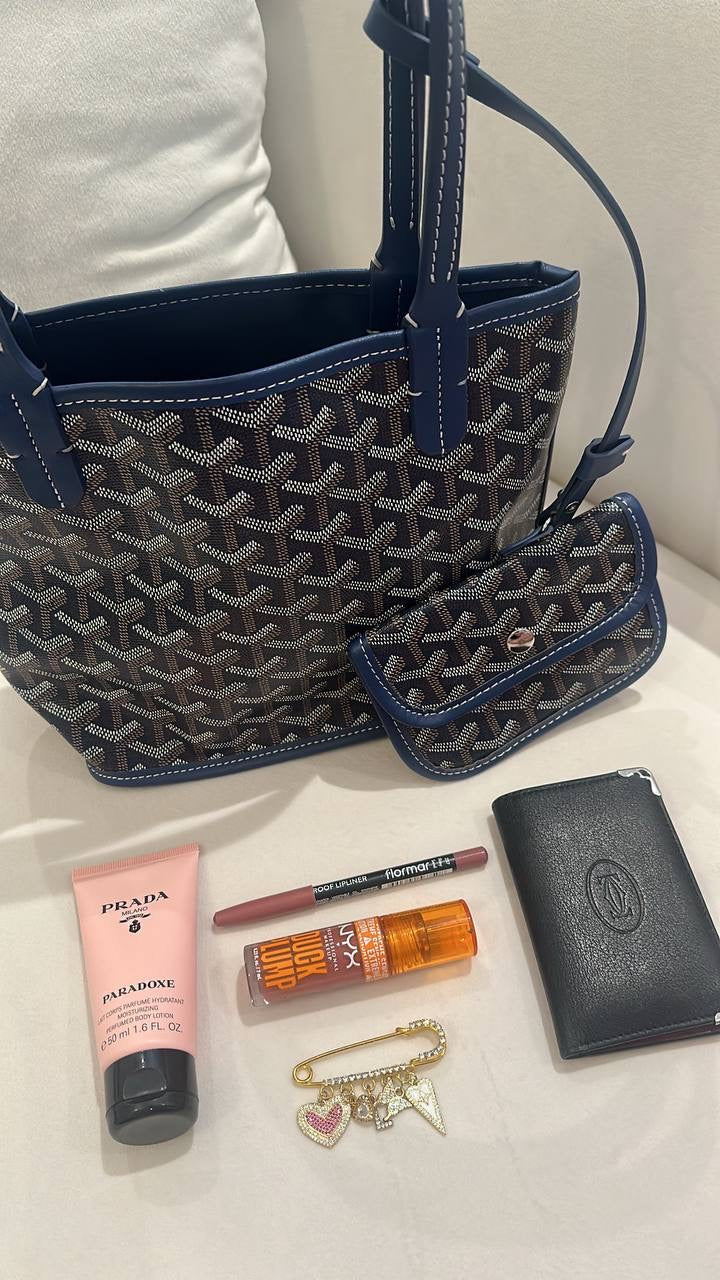 Blue patterned handbag with Prada lotion, lipstick, and wallet on a white surface
