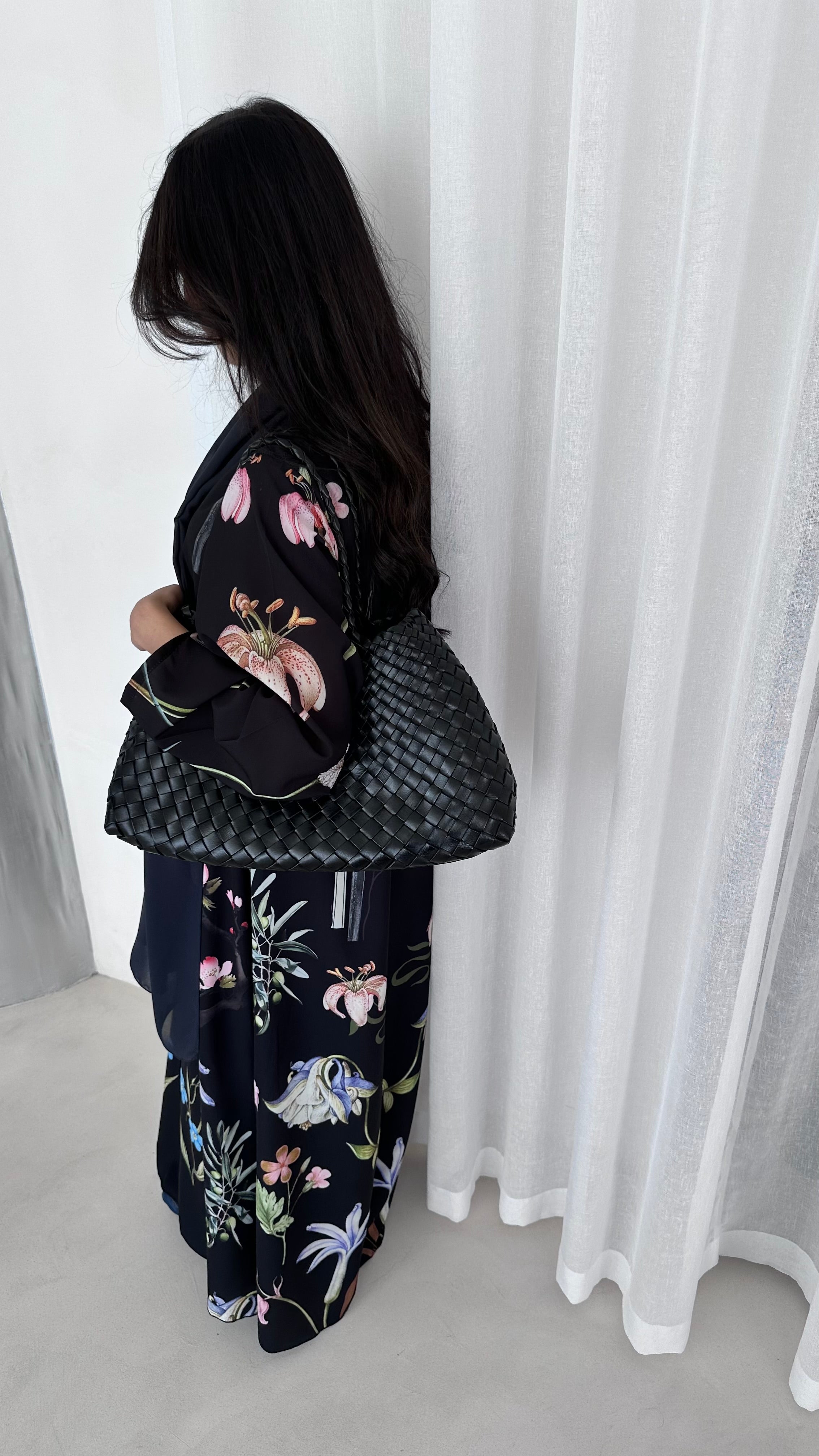 Person wearing a black floral kimono standing against a white curtain.
