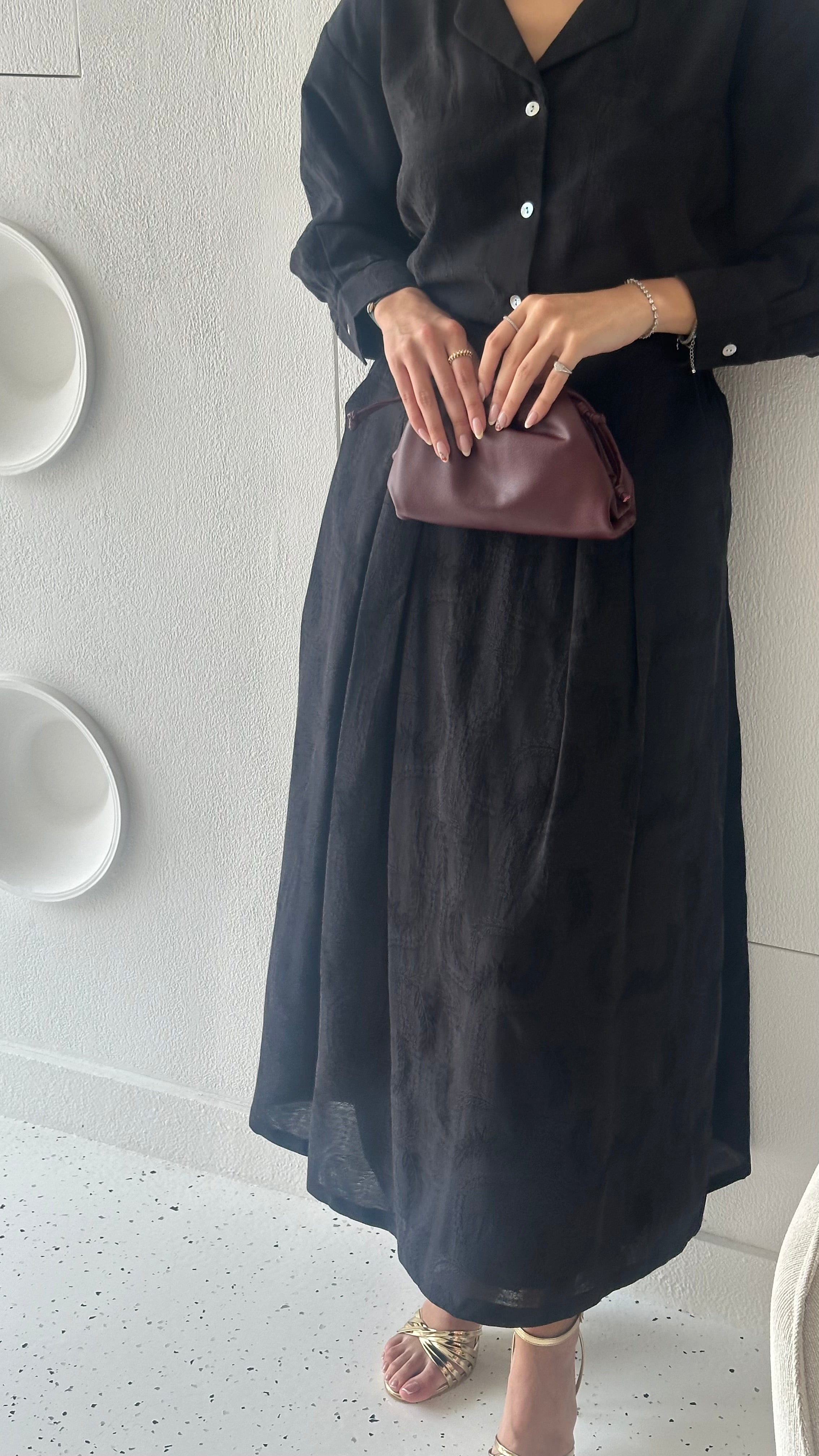 A person holding a maroon-colored pouch with a black dress in the background.