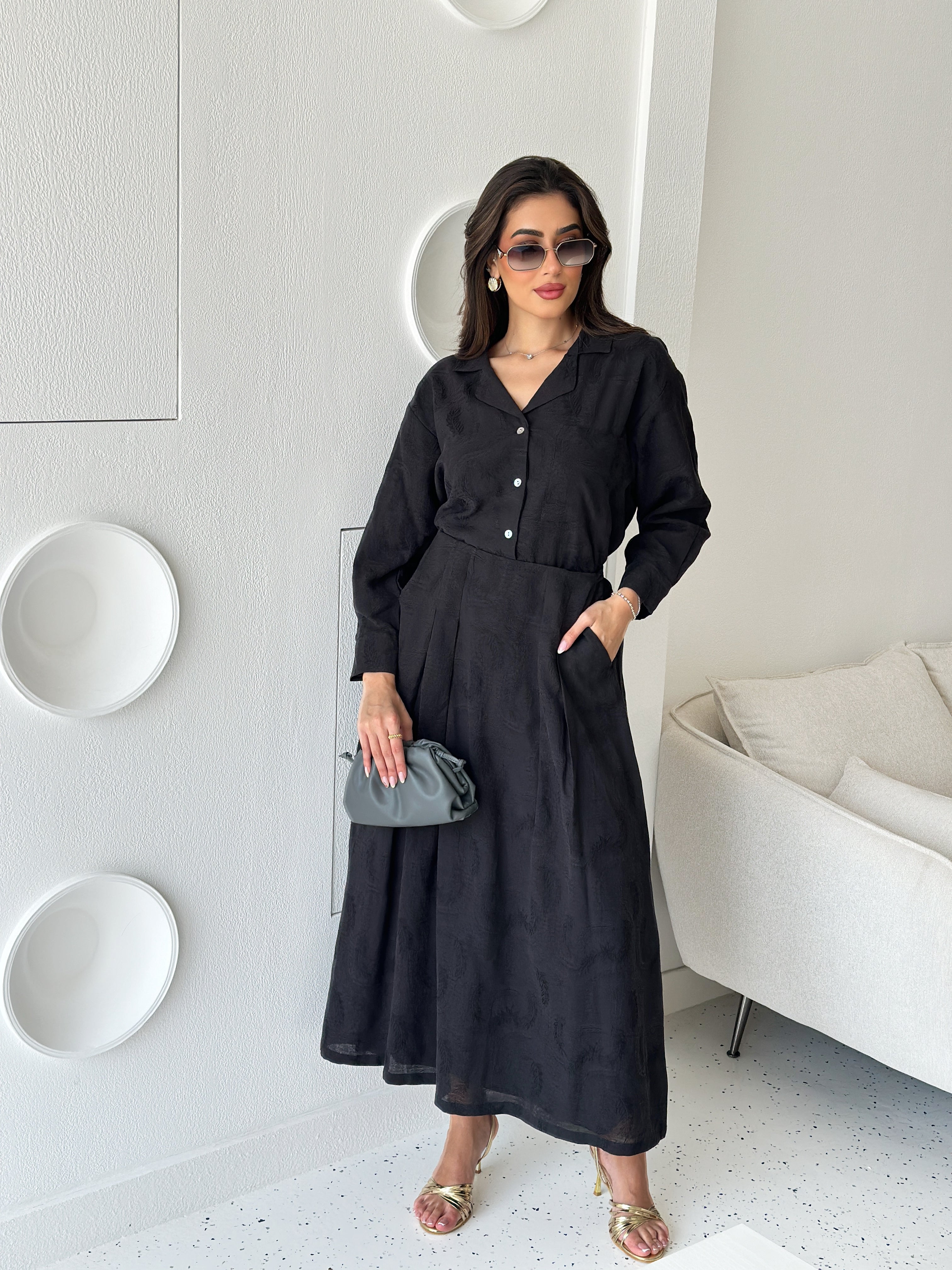 A person wearing a black dress is holding a grey pouch with a long strap.