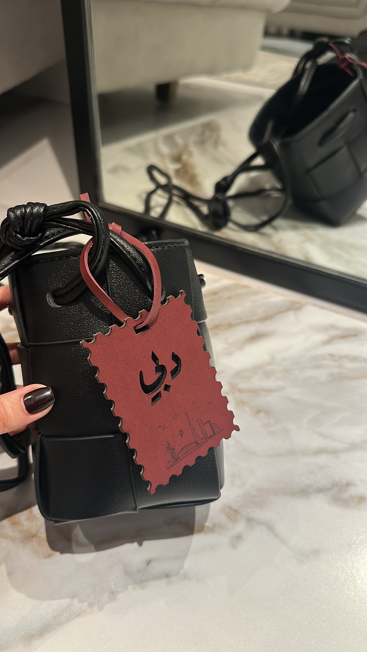 Black electronic device with a red tag held by a hand on a marble surface.