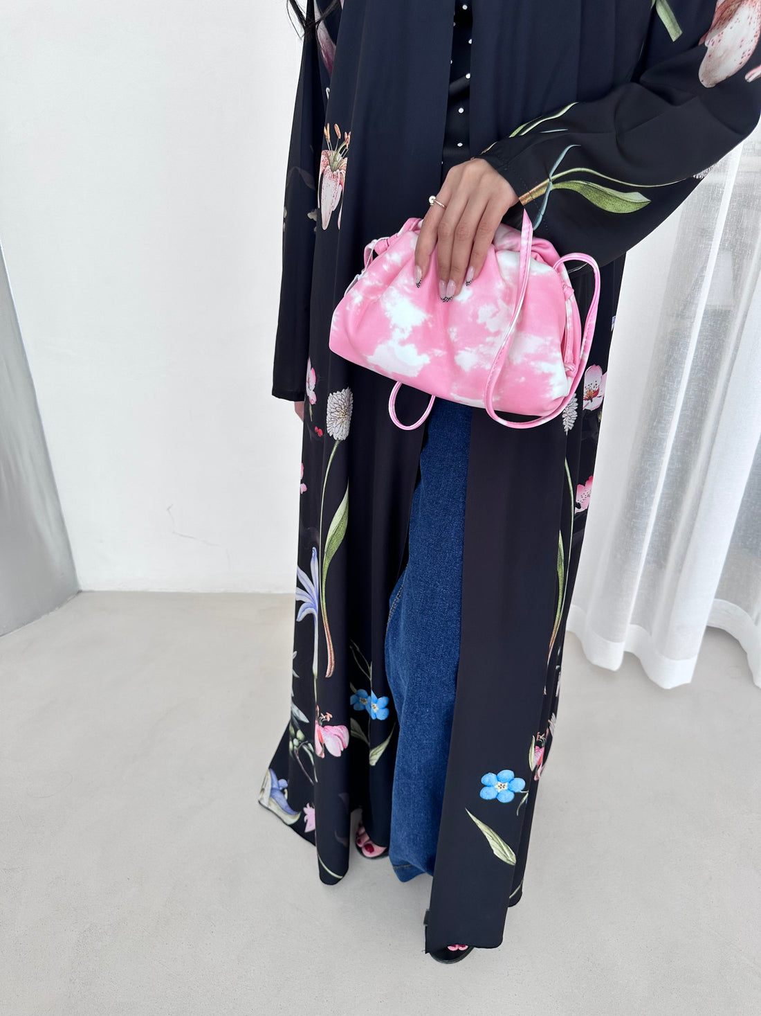 Person holding a pink floral bag with folded clothes on a white background