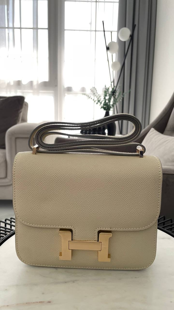 Beige handbag with gold clasp on a table in a room with large windows.