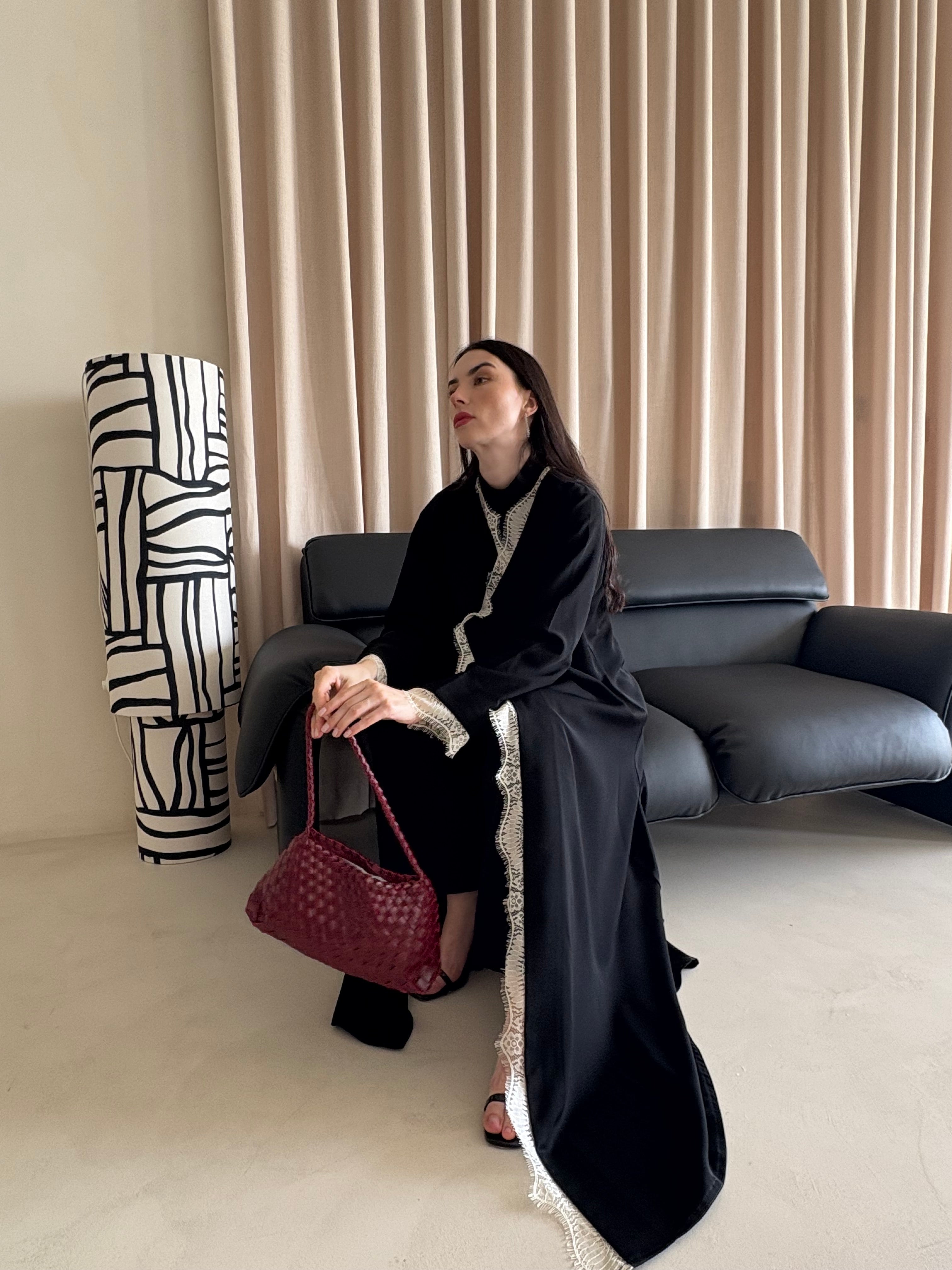 Woman in a black abaya holding a red handbag in a living room setting.