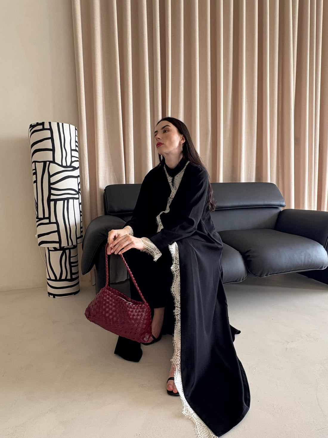 Woman in a black abaya holding a red handbag in a living room setting.