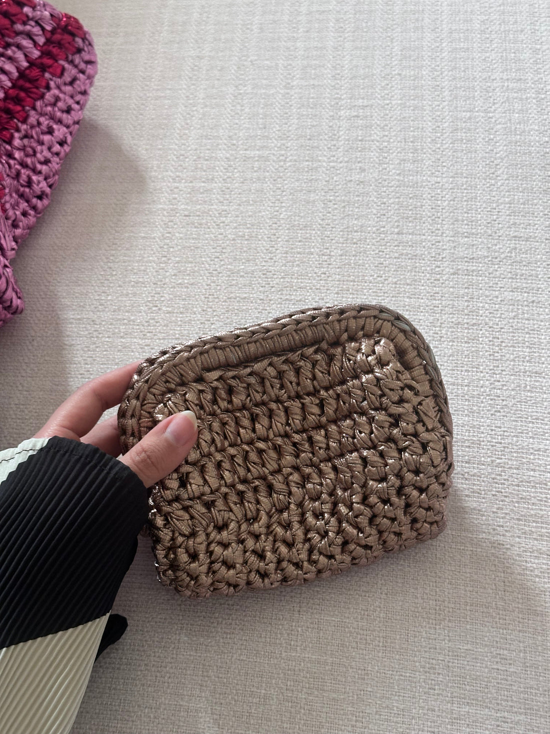 Hand holding a woven brown pouch on a light gray surface