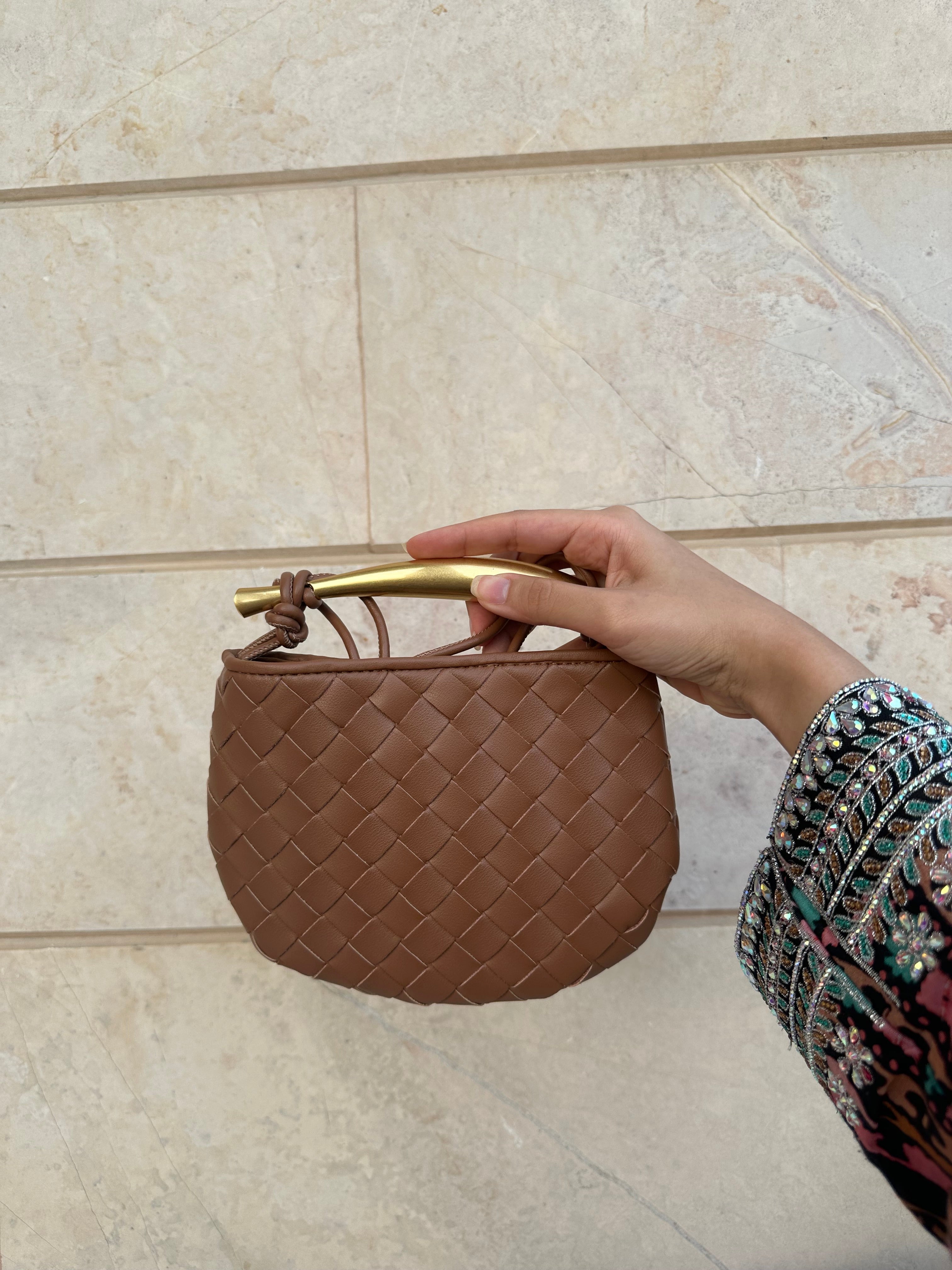 A person holding a small brown handbag with a textured surface and a gold-colored chain strap.
