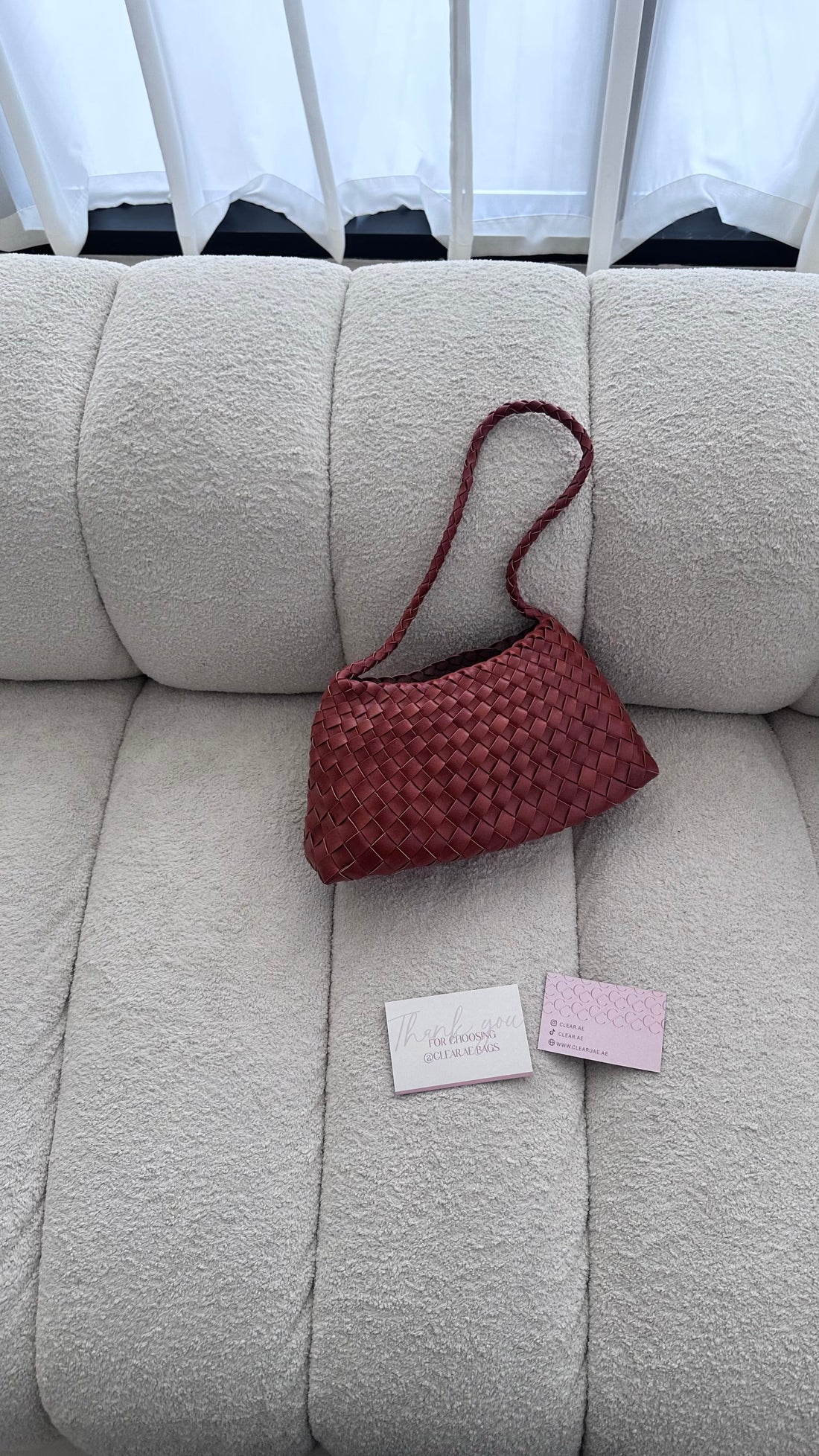 Red woven handbag on a beige couch with two pink labels.