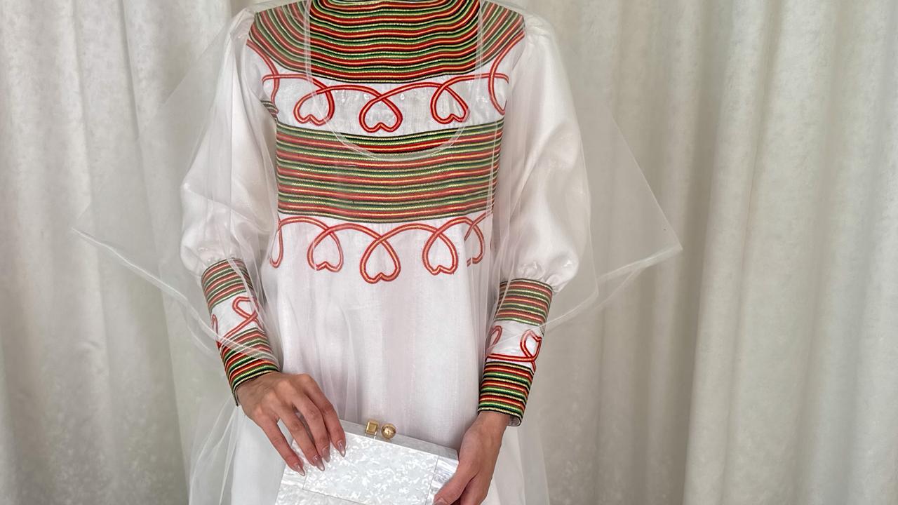 Traditional outfit with a white blouse and colorful patterned sleeves against a plain background