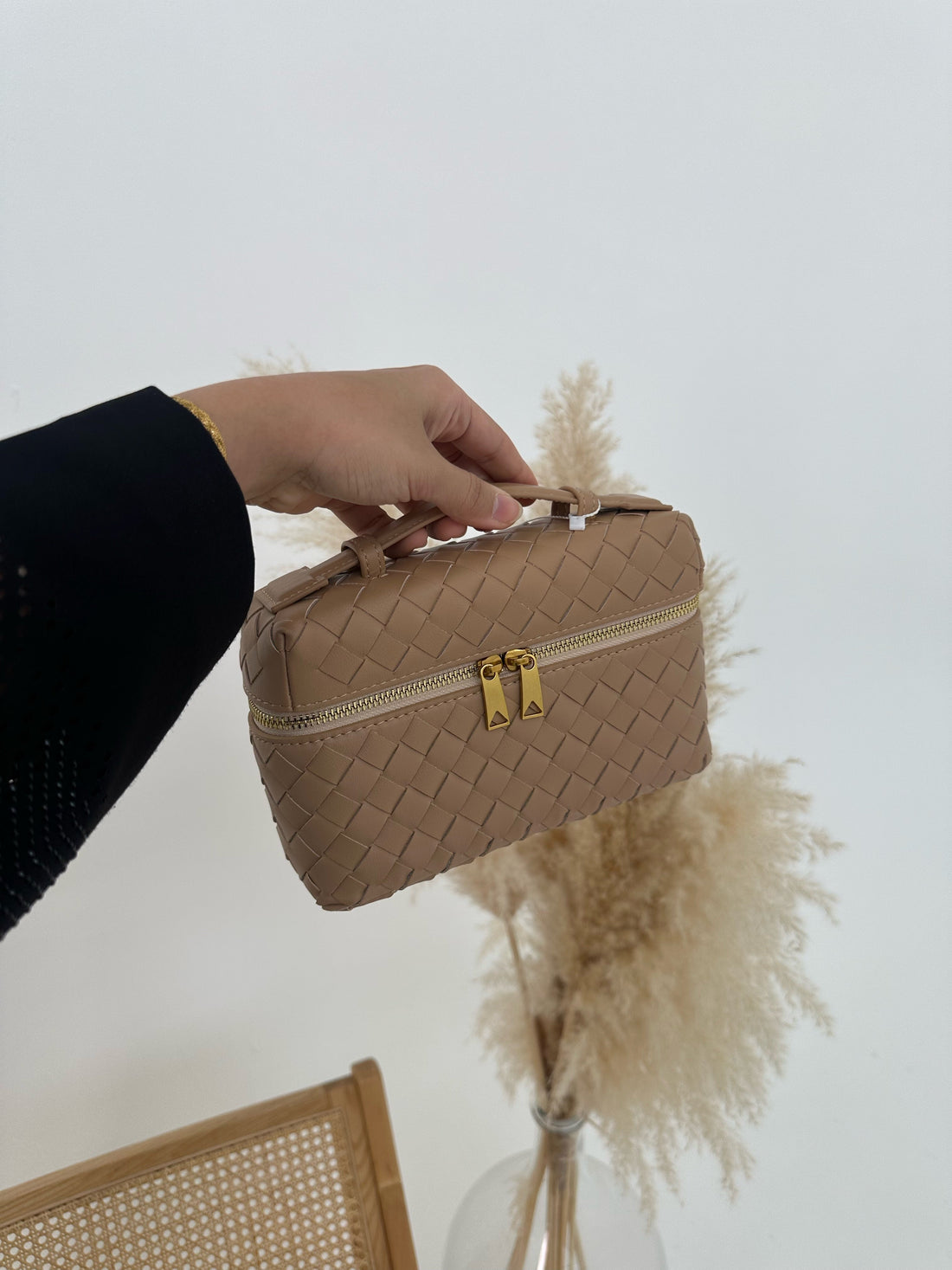 Person holding a beige woven makeup bag with a gold zipper against a neutral background