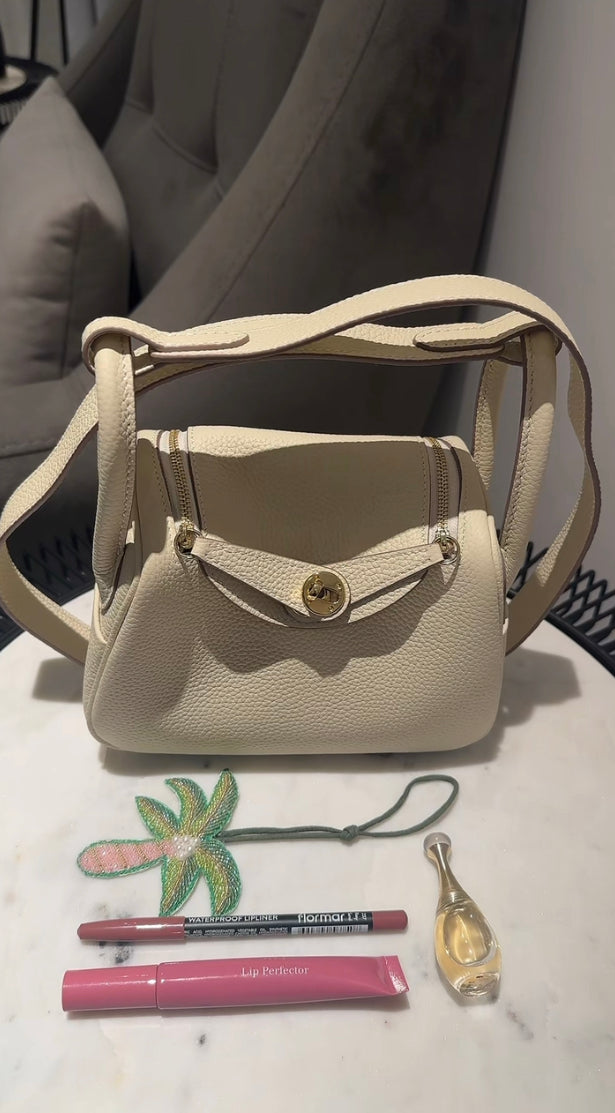 Small beige handbag on a white surface with makeup items and a keychain.