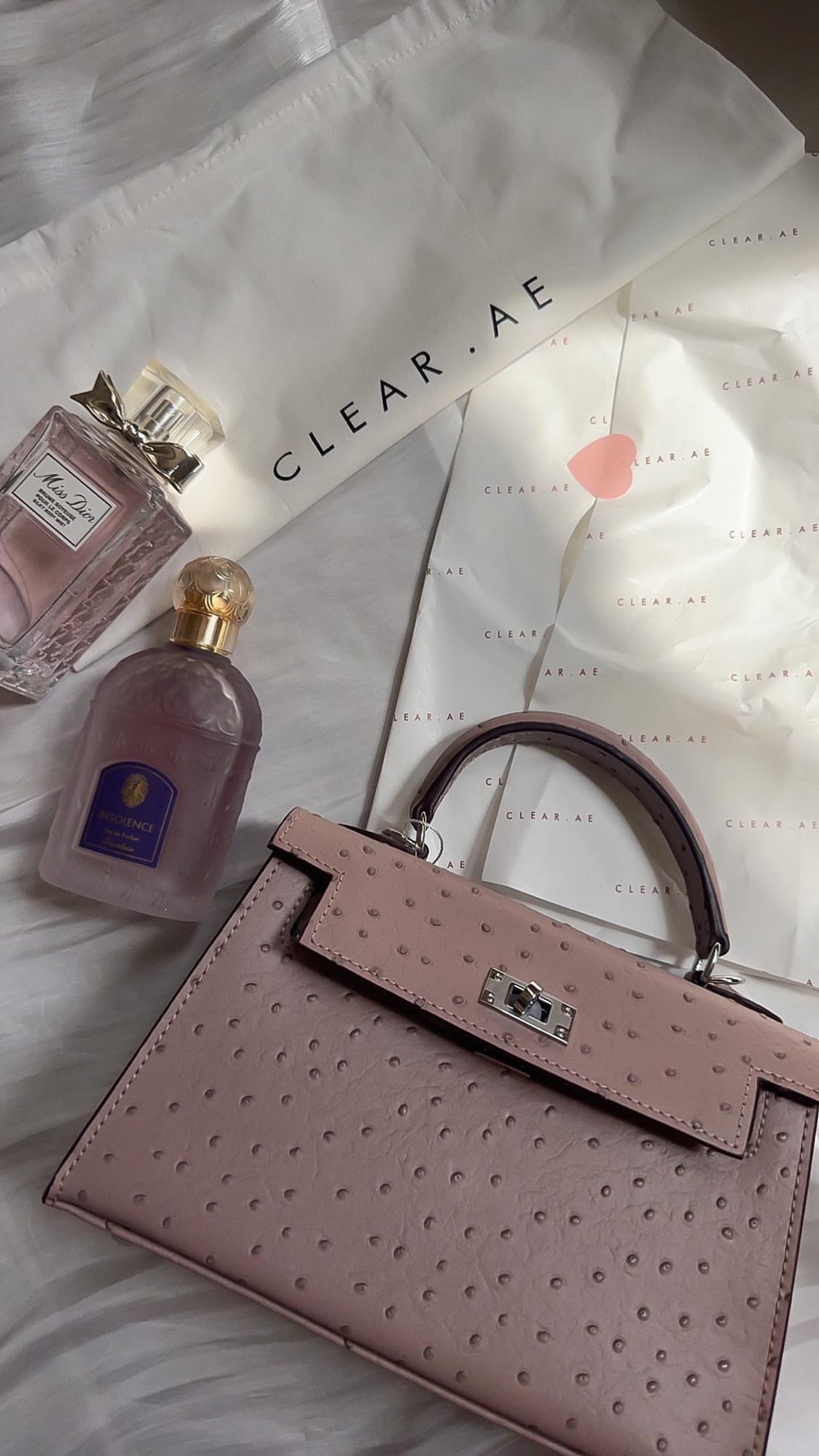 Pink handbag with two bottles of perfume on a light background