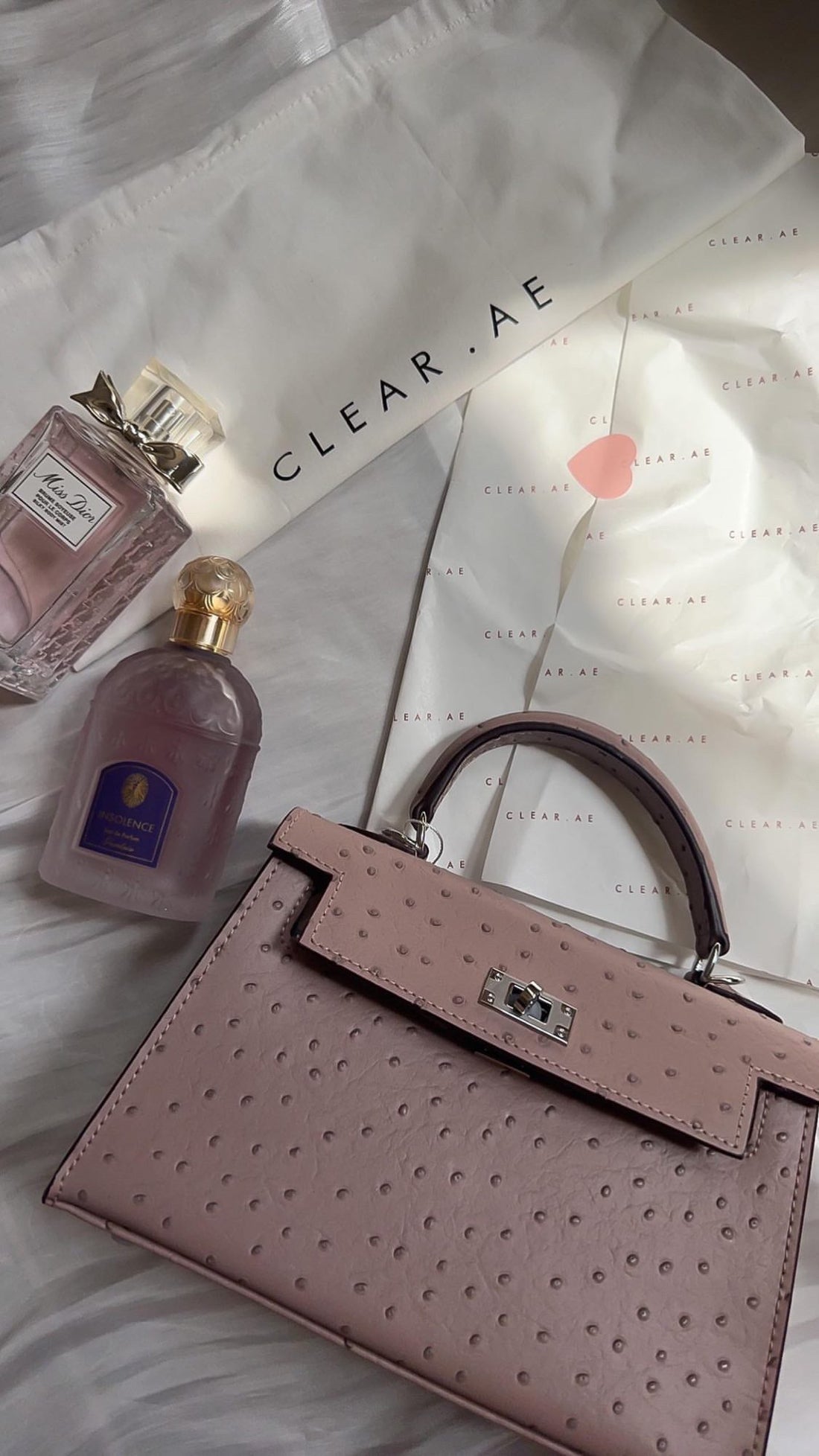 Pink handbag with two bottles of perfume on a light background