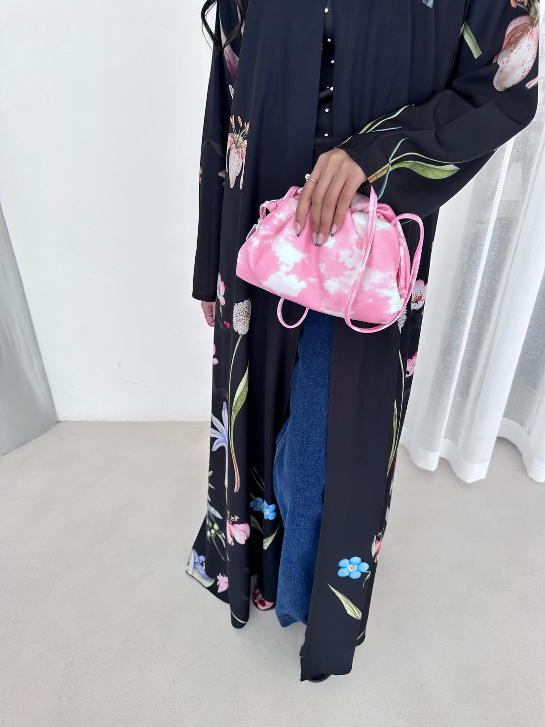 Person holding a pink floral bag with a stack of folded clothes on a white background