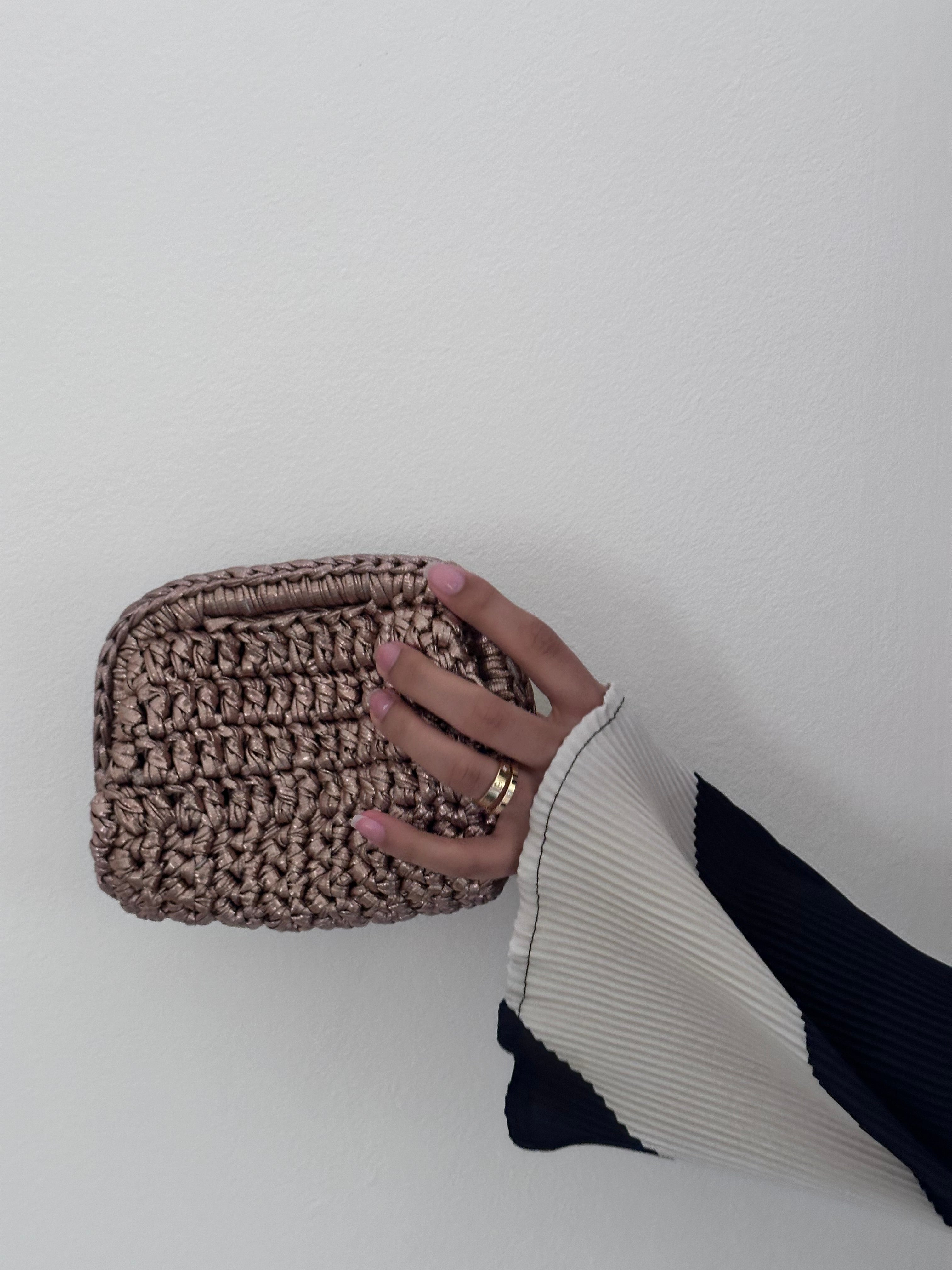 Hand holding a woven brown pouch against a plain background