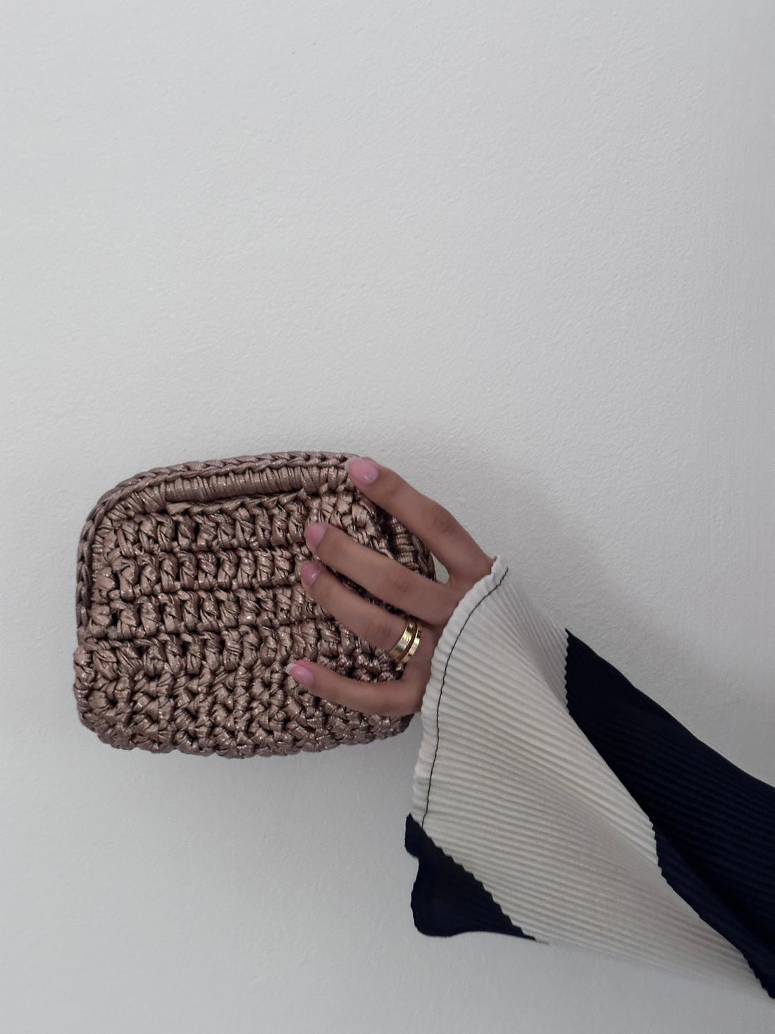 Hand holding a woven brown pouch against a plain background