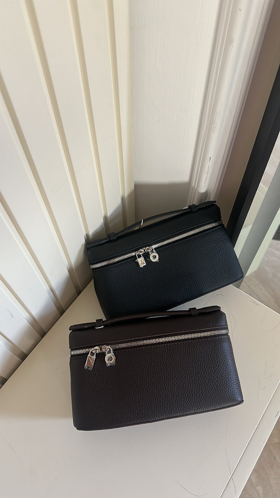 Two black handbags with silver zippers on a light-colored surface.