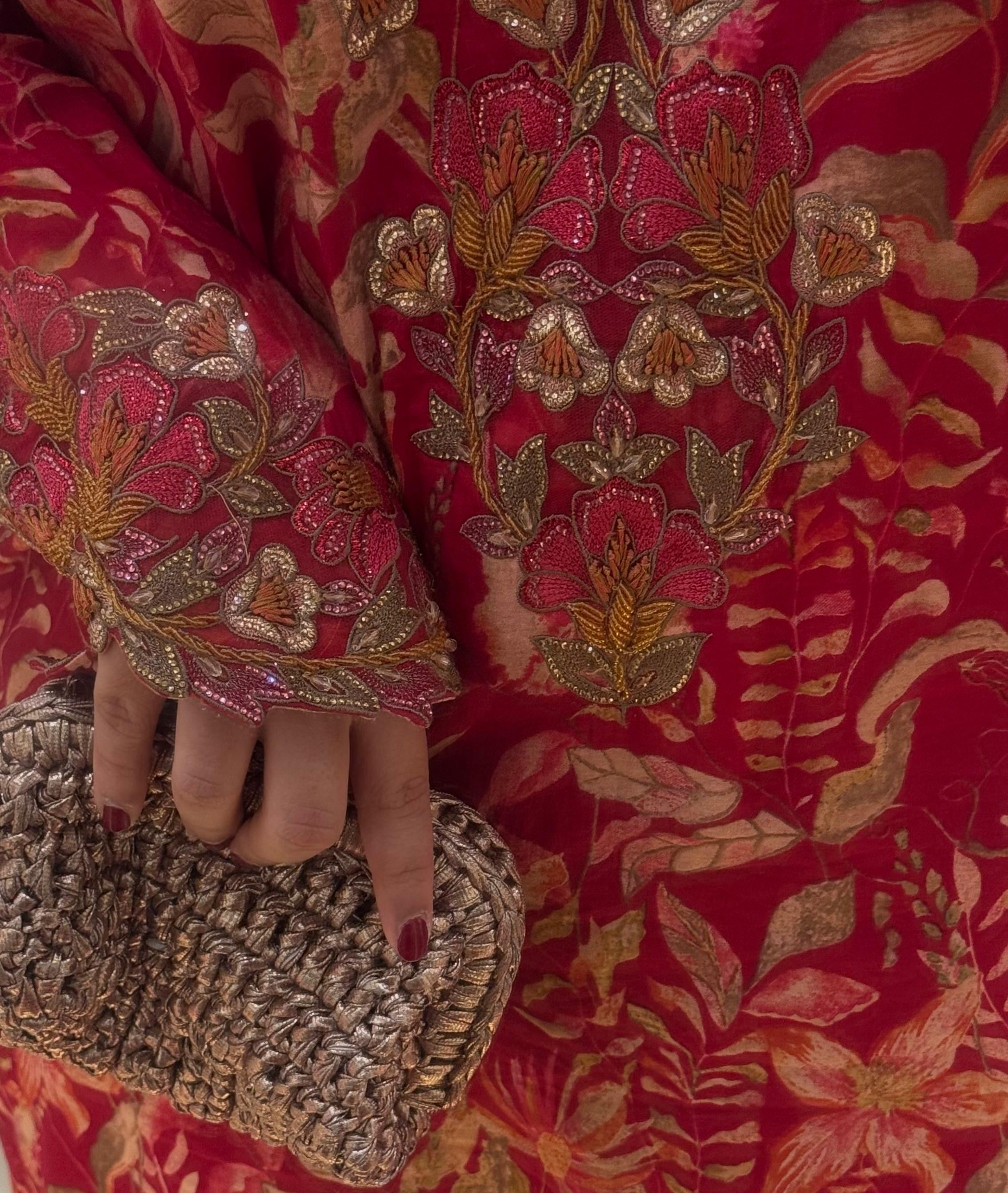 Person wearing a red embroidered outfit holding a textured clutch.